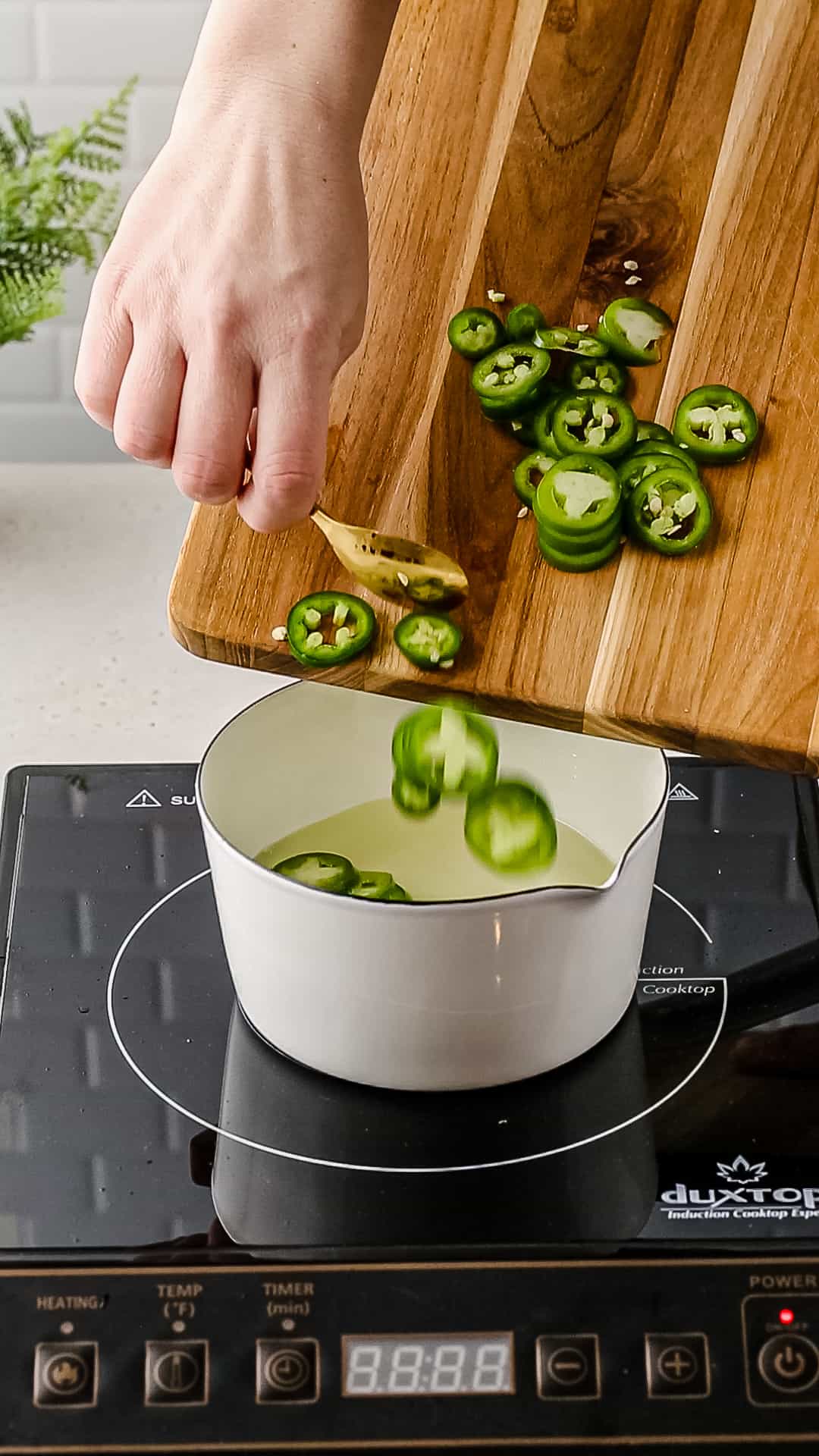 Adding sliced fresh jalapenos to a saucepan.