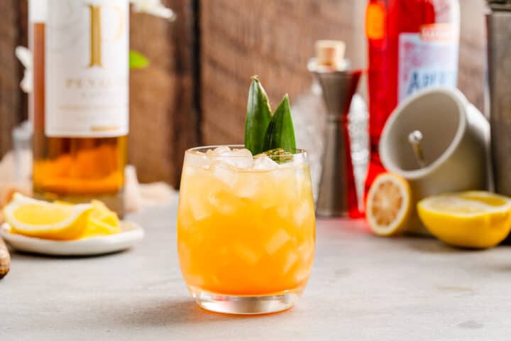 Pineapple Bourbon Whiskey Smash with pineapple fronds as garnish and ingredients in the background.