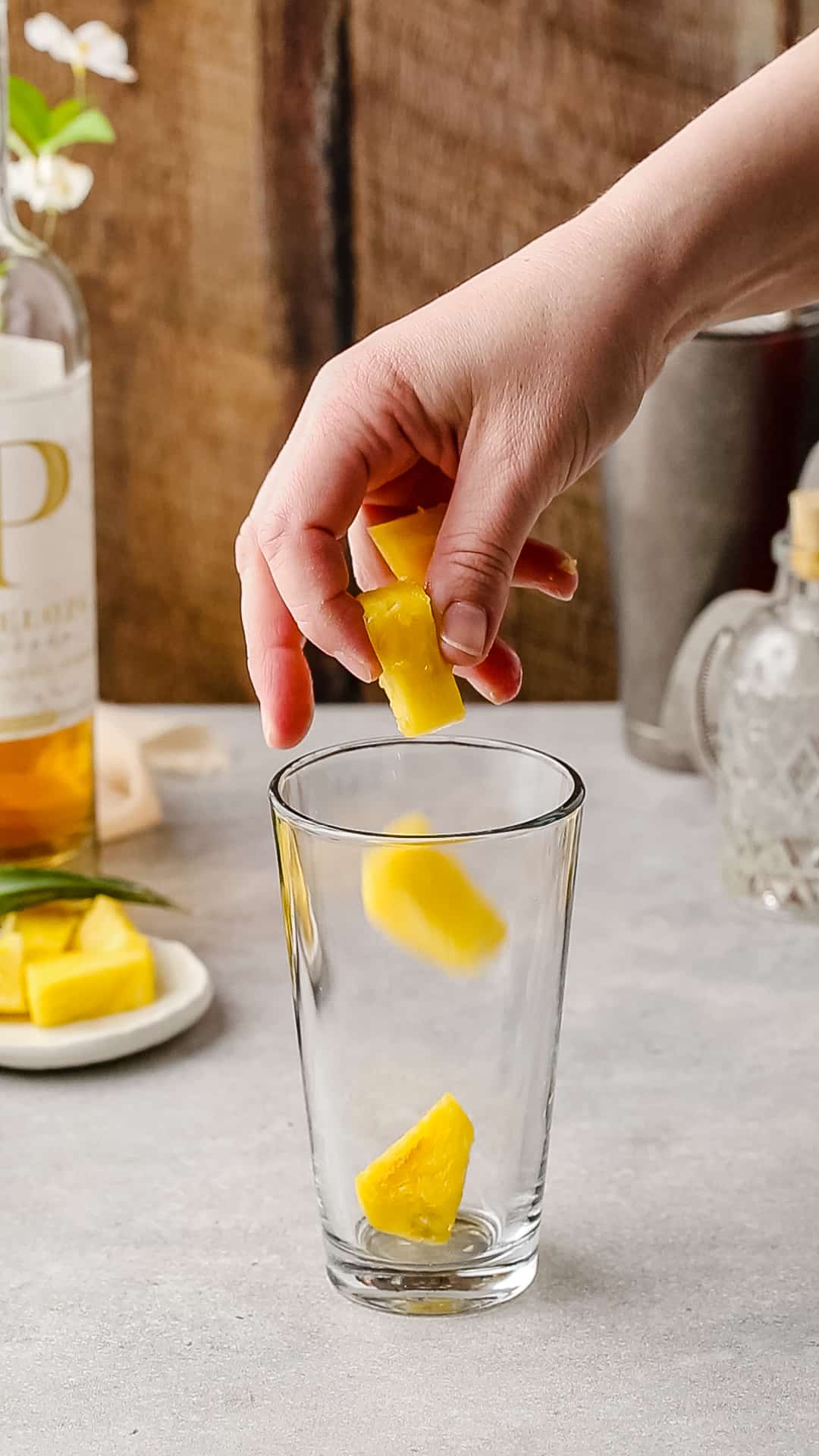 Hand adding pineapple chunks to a cocktail shaker.