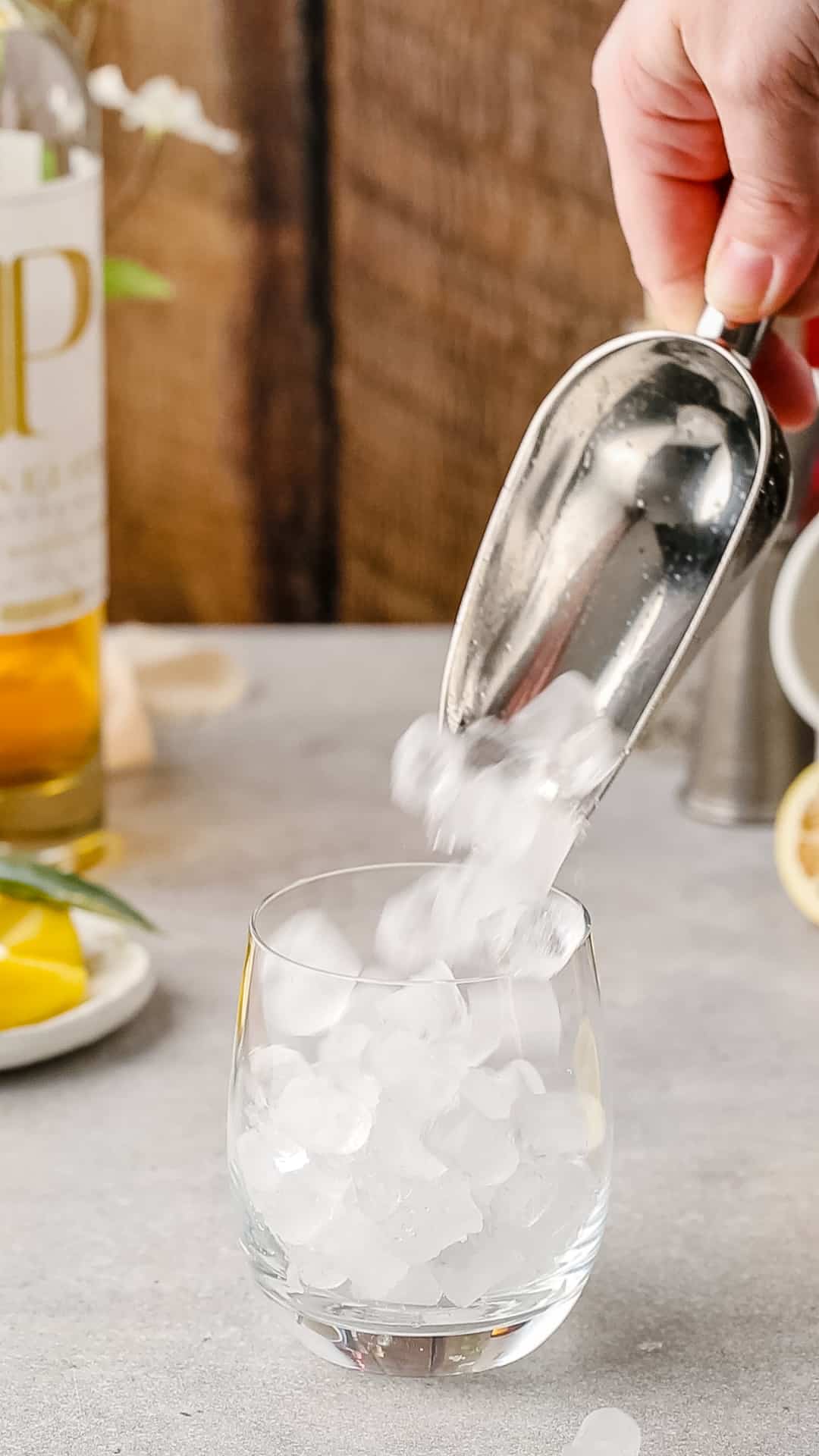 Adding ice to a cocktail serving glass using a metal ice scoop.