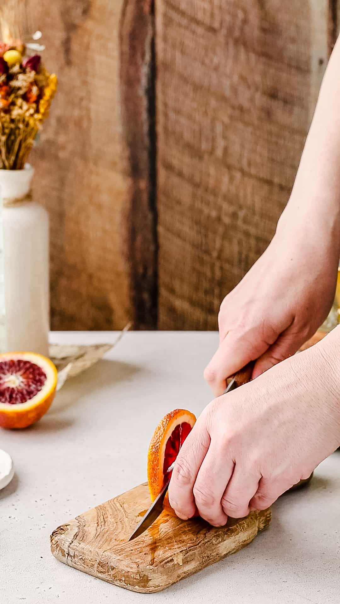Hands slicing a blood orange on a cutting board.