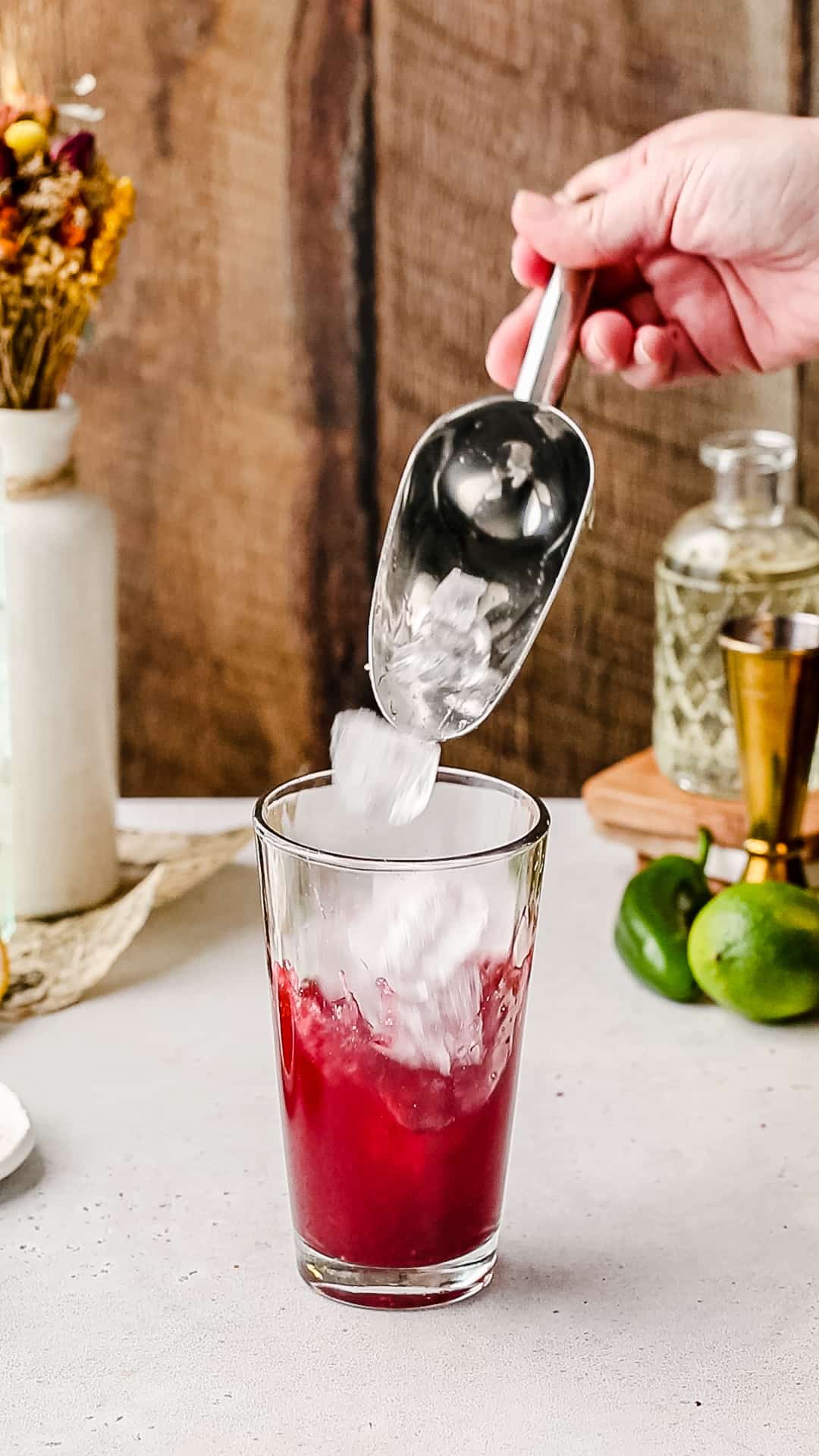 Filling a cocktail shaker with ice using an ice scoop.
