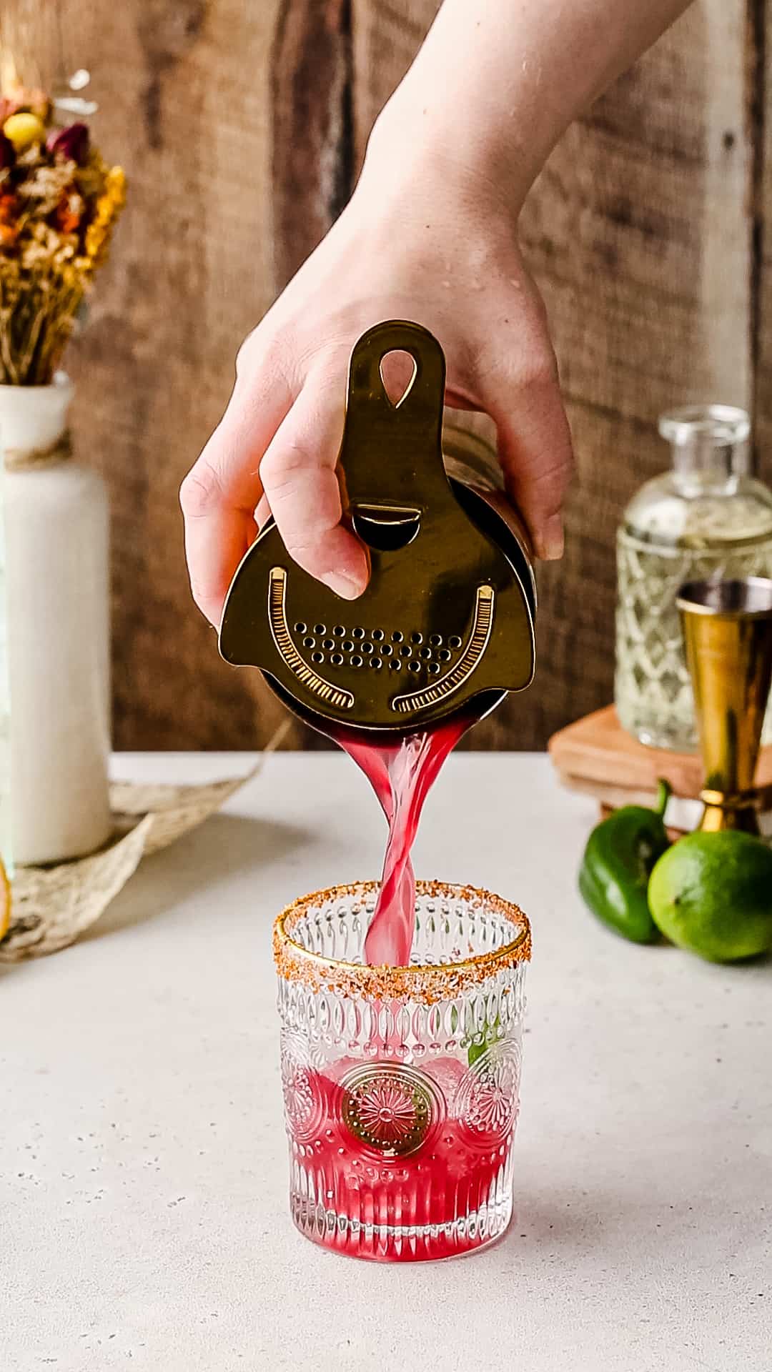 Straining a red colored drink into a cocktail glss.