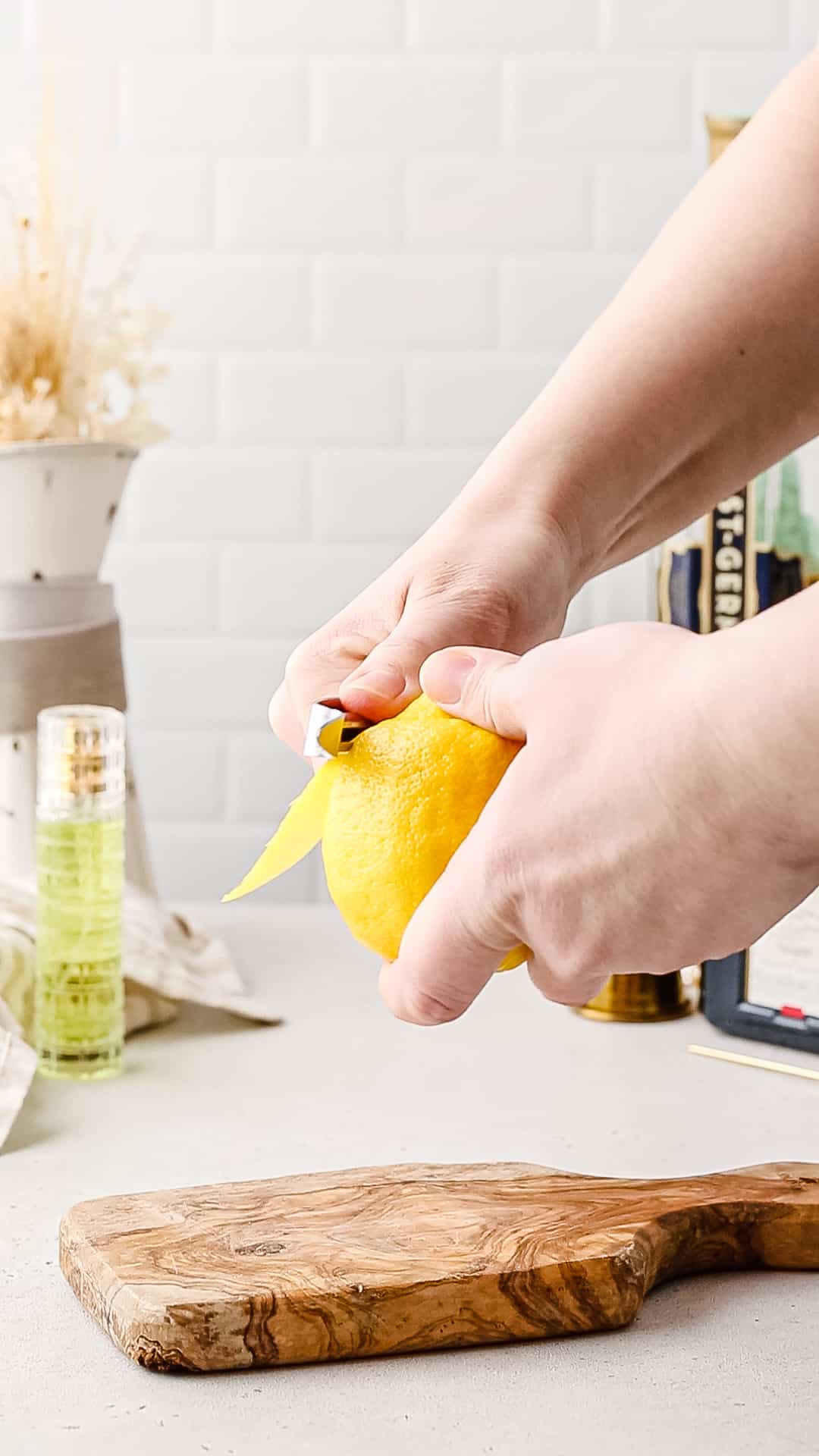 Hands using a vegetable peeler to peel a lemon.
