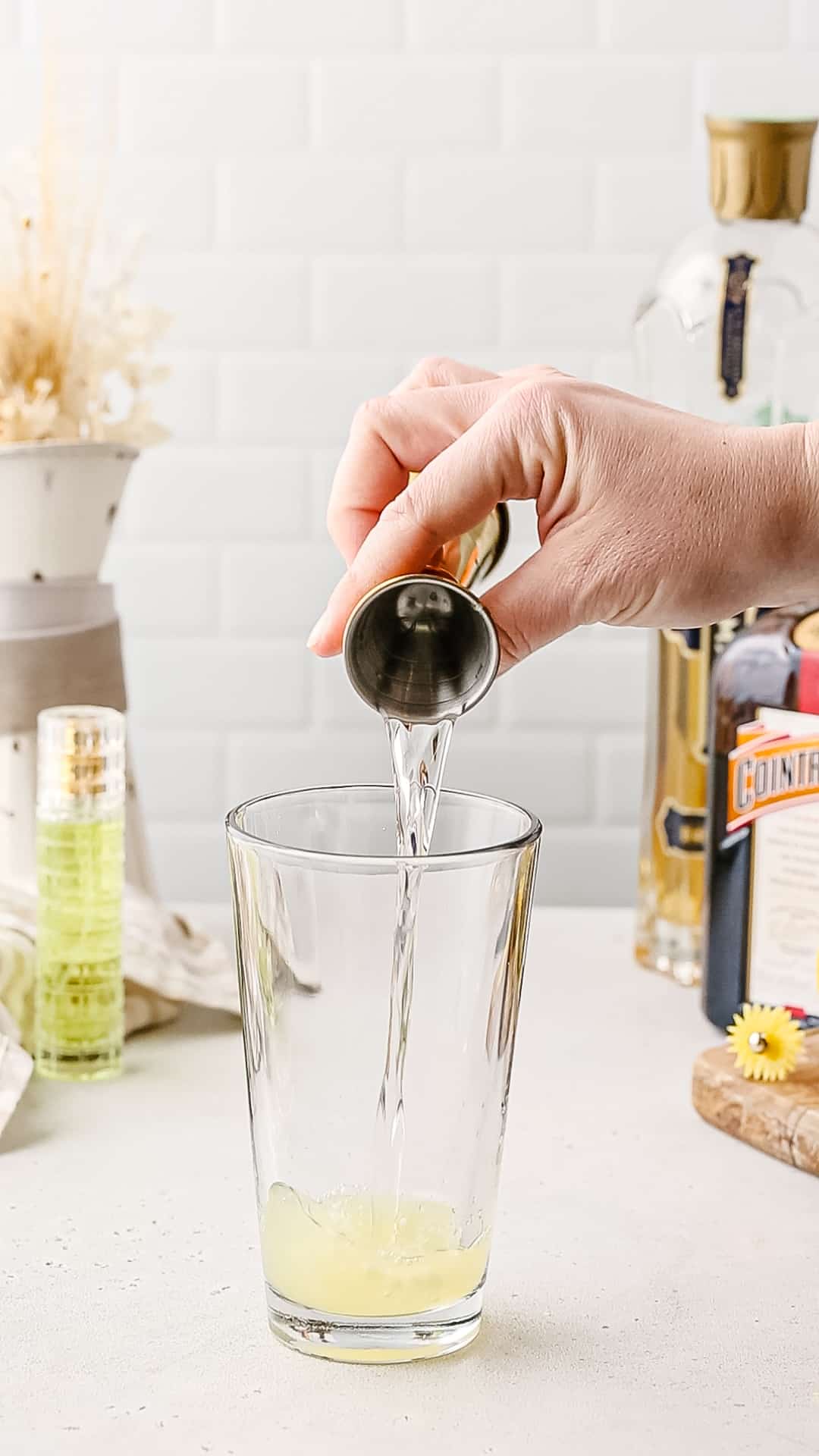 Hand pouring Cointreau liqueur from a jigger into a cocktail shaker.