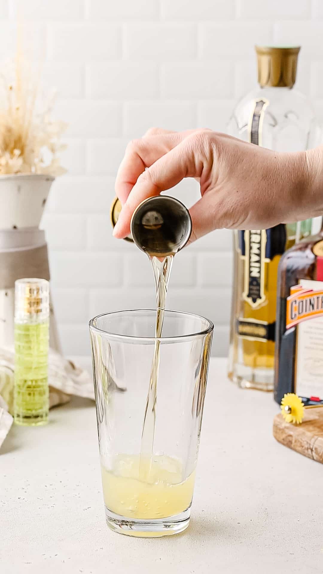 Hand pouring St Germain liqueur into a cocktail shaker.