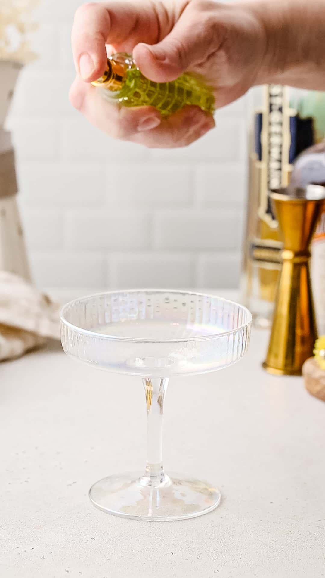 Hand using a spray bottle to add absinthe to the inside of a cocktail glass.