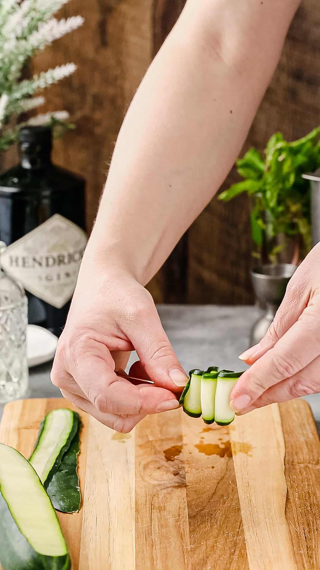 Hands making a zigzag of a cucumber strip and threading it onto a cocktail pick.