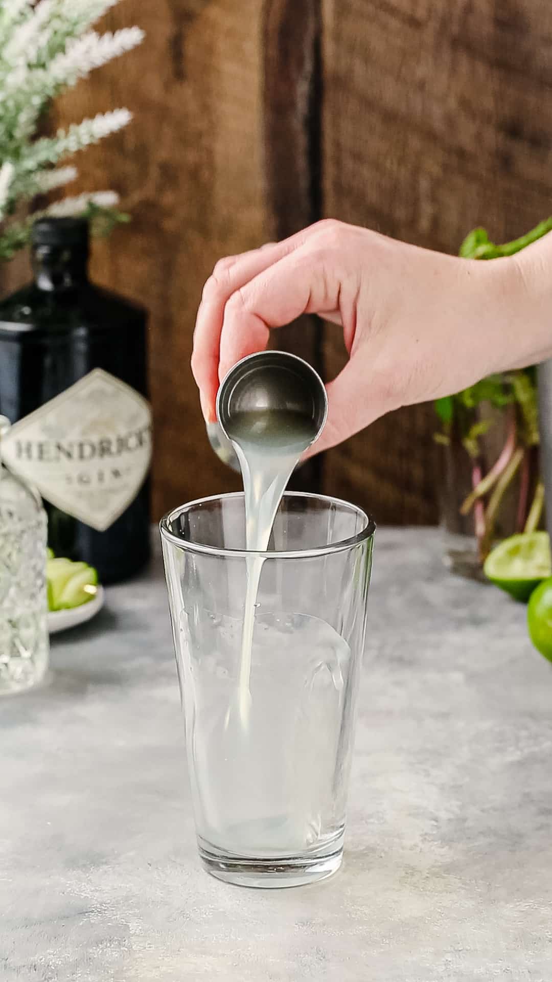Hand adding lime juice to a cocktail shaker using a jigger.