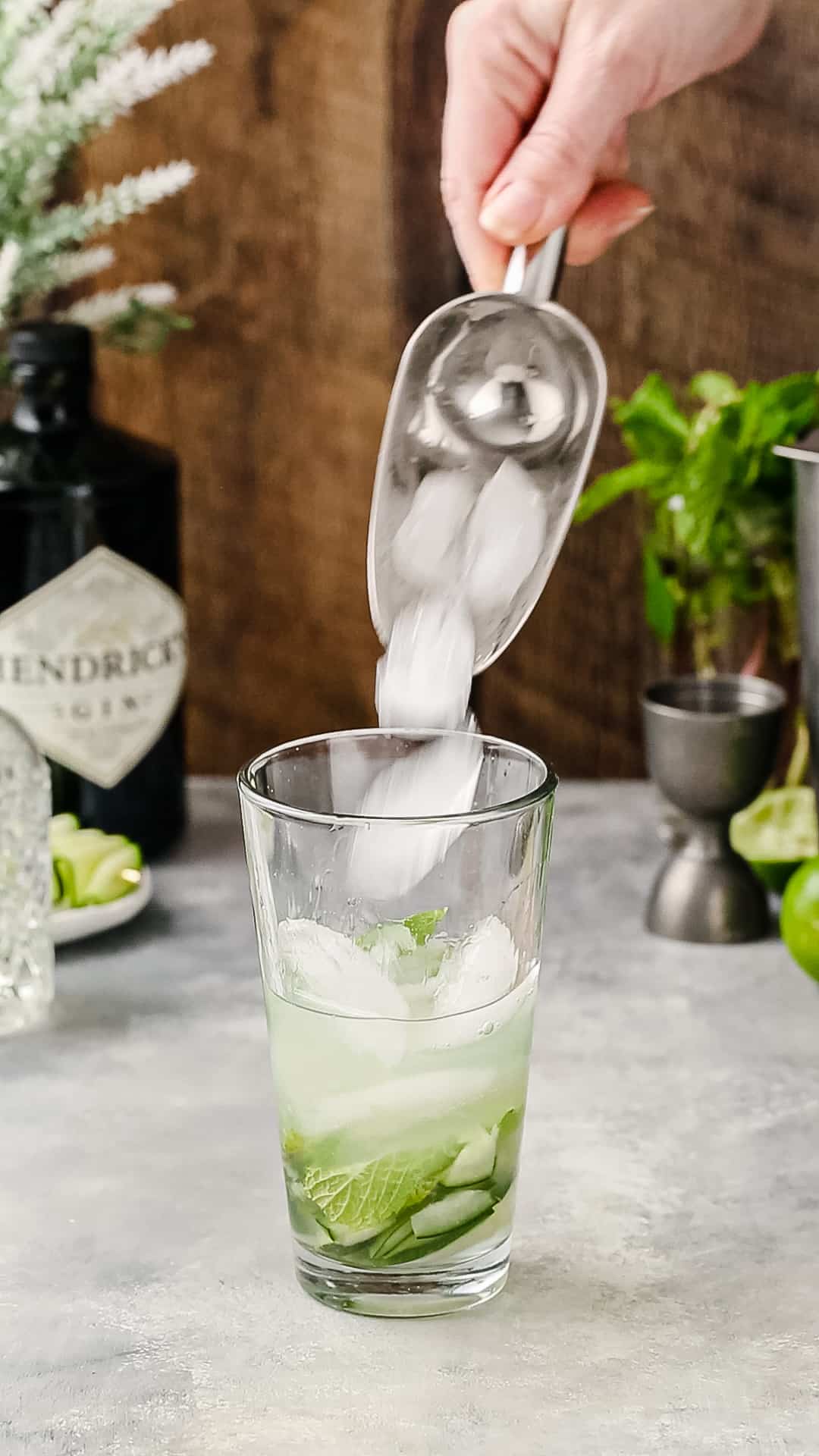 Hand using an ice scoop to add ice to a cocktail shaker.