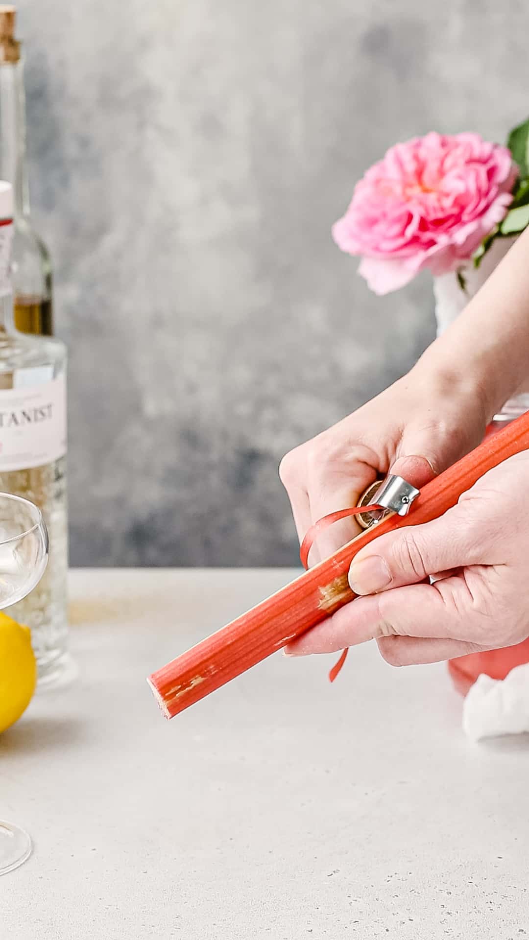 Hand using a vegetable peeler to peel off a strip of rhubarb skin.