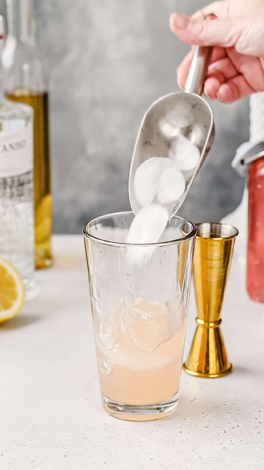Hand using a metal scoop to add ice to a cocktail shaker.