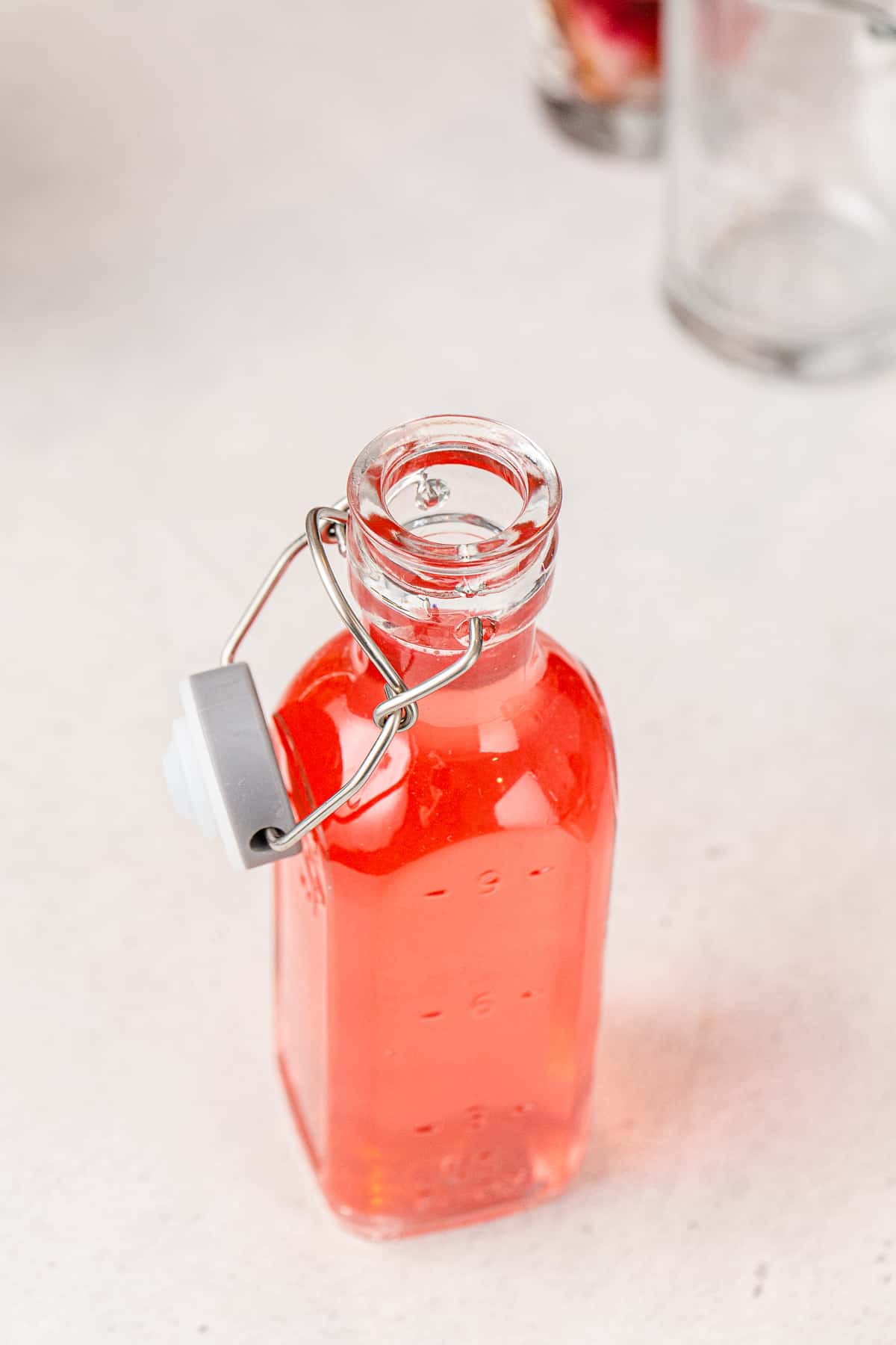 Glass swing-top bottle filled with pink rhubarb syrup, sitting open on a countertop.