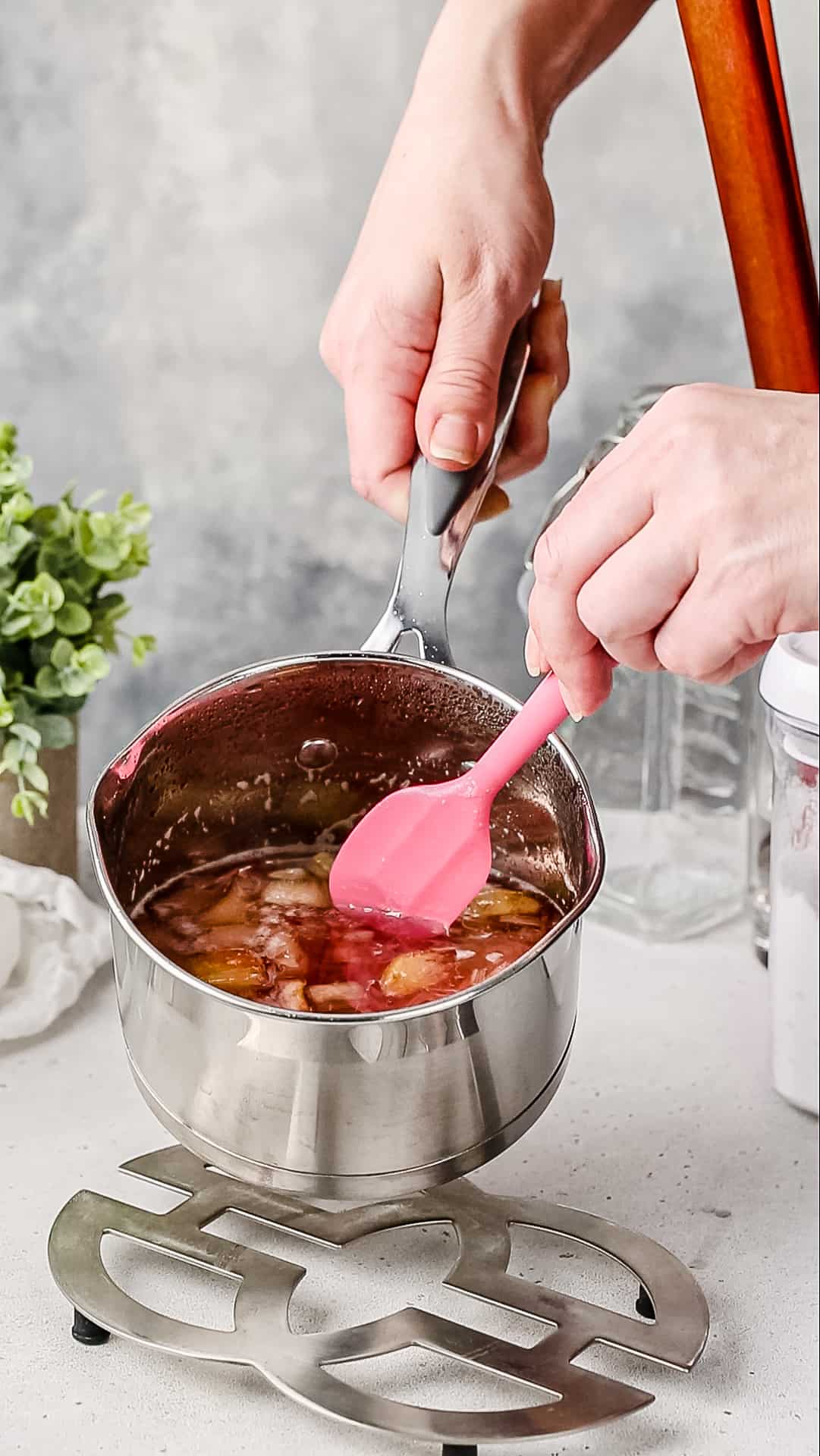 Hands using a spatula to show how the rhubarb is cooked and breaking into strands in the saucepan.