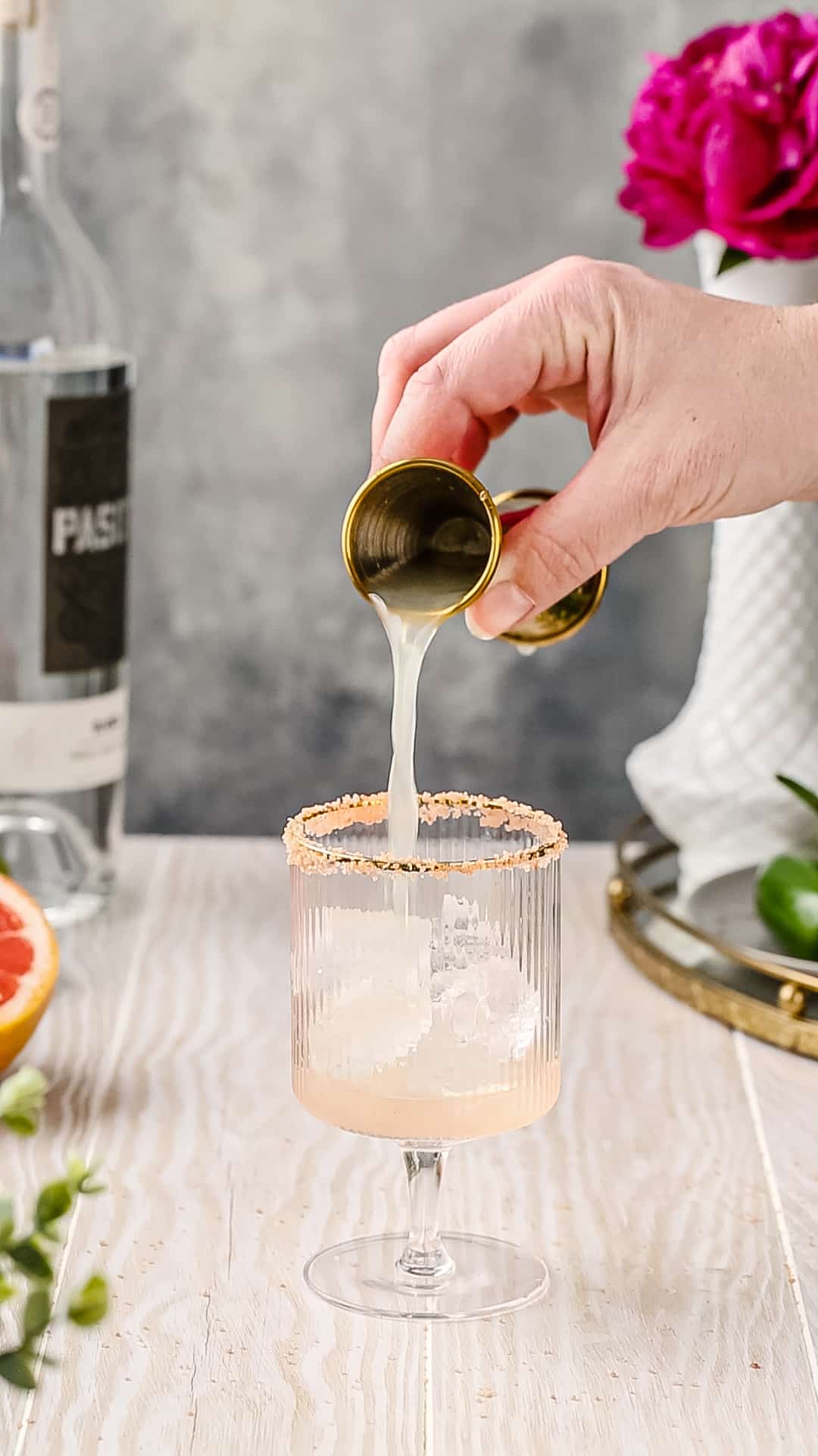 Using a jigger to pour lime juice into a cocktail glass.