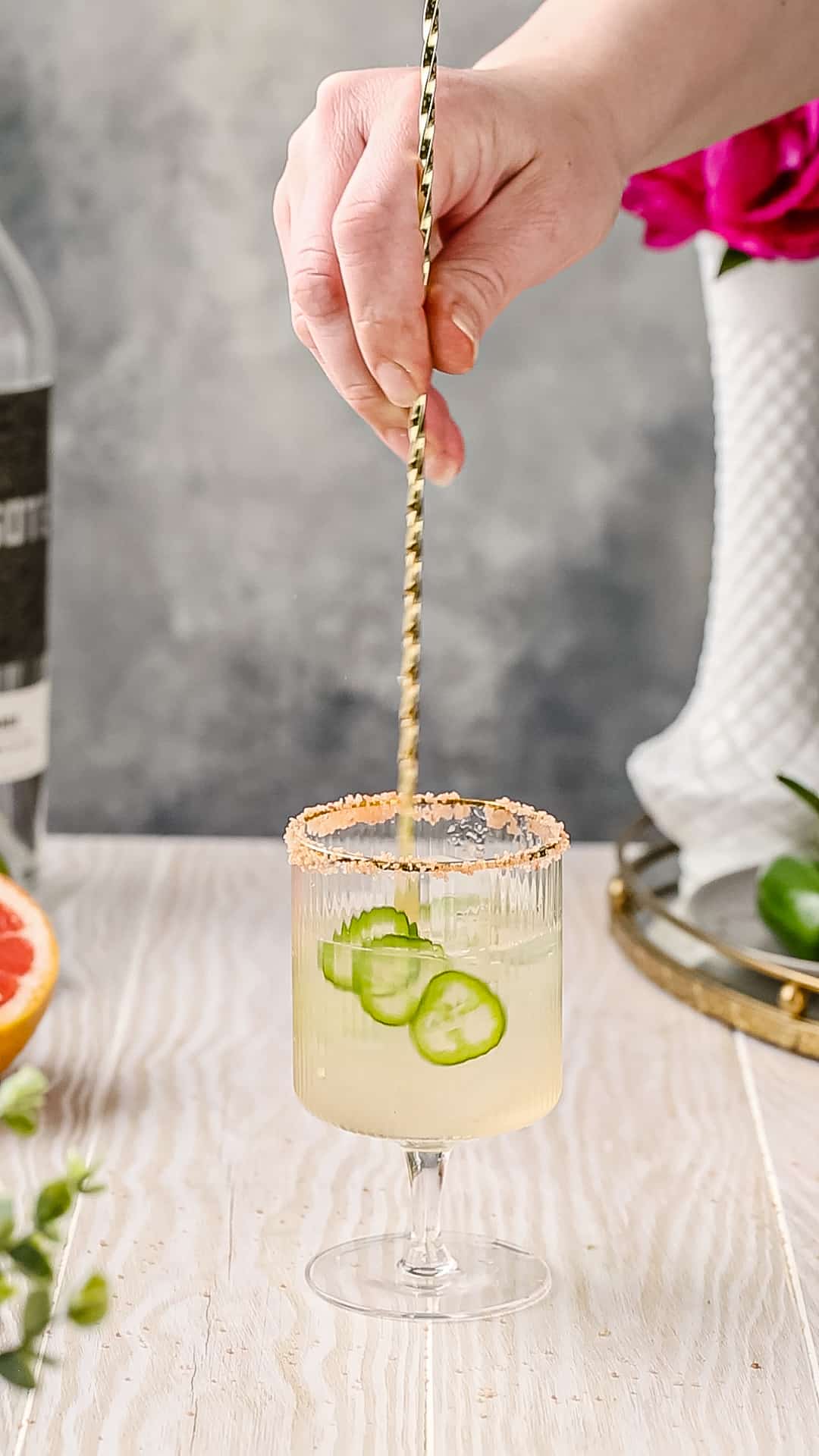 Stirring jalapeno slices into the cocktail glass.