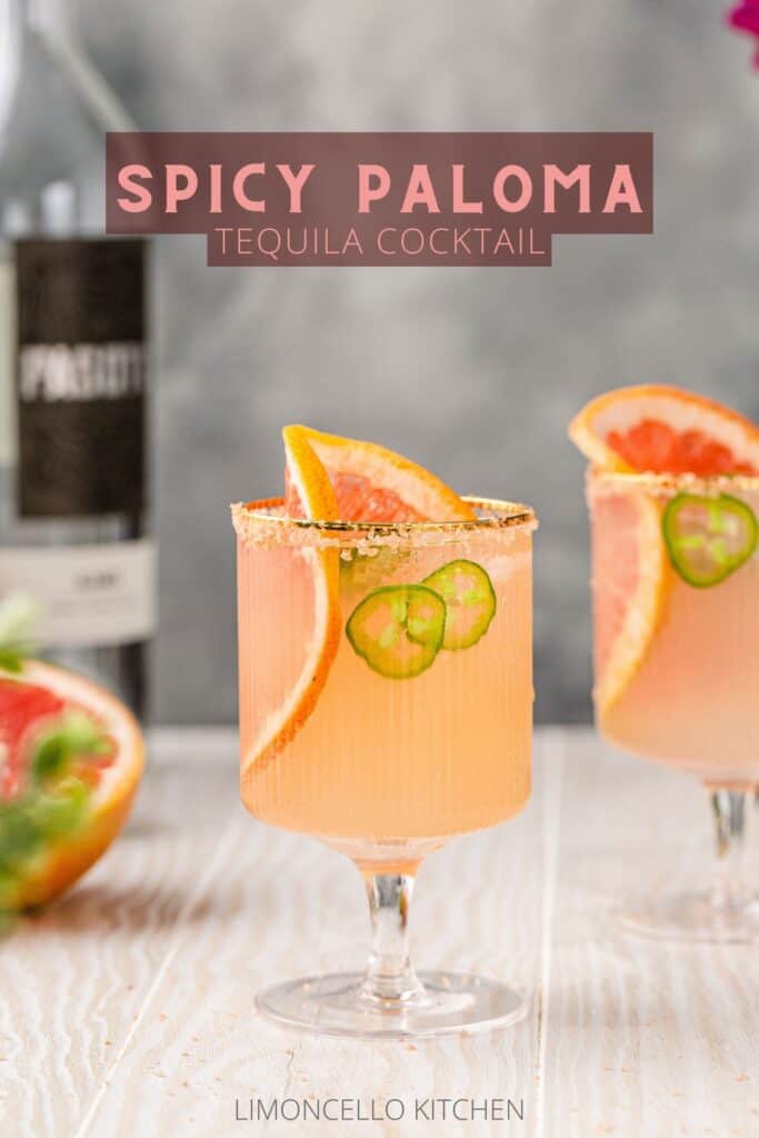 Two Spicy Paloma cocktails on a white wooden countertop with tequila and grapefruit in the background and the text "Spicy Paloma Tequila Cocktail" on top.