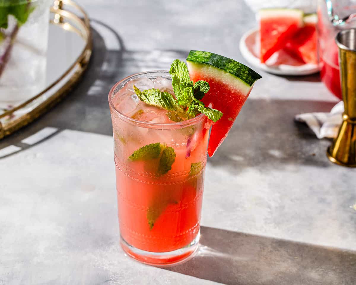 Watermelon Mojito on a countertop with watermelon slices and bar tools in the background.