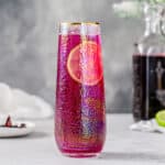 Side view of pink HIbiscus gin cocktail with a lime wheel garnish inside the glass.