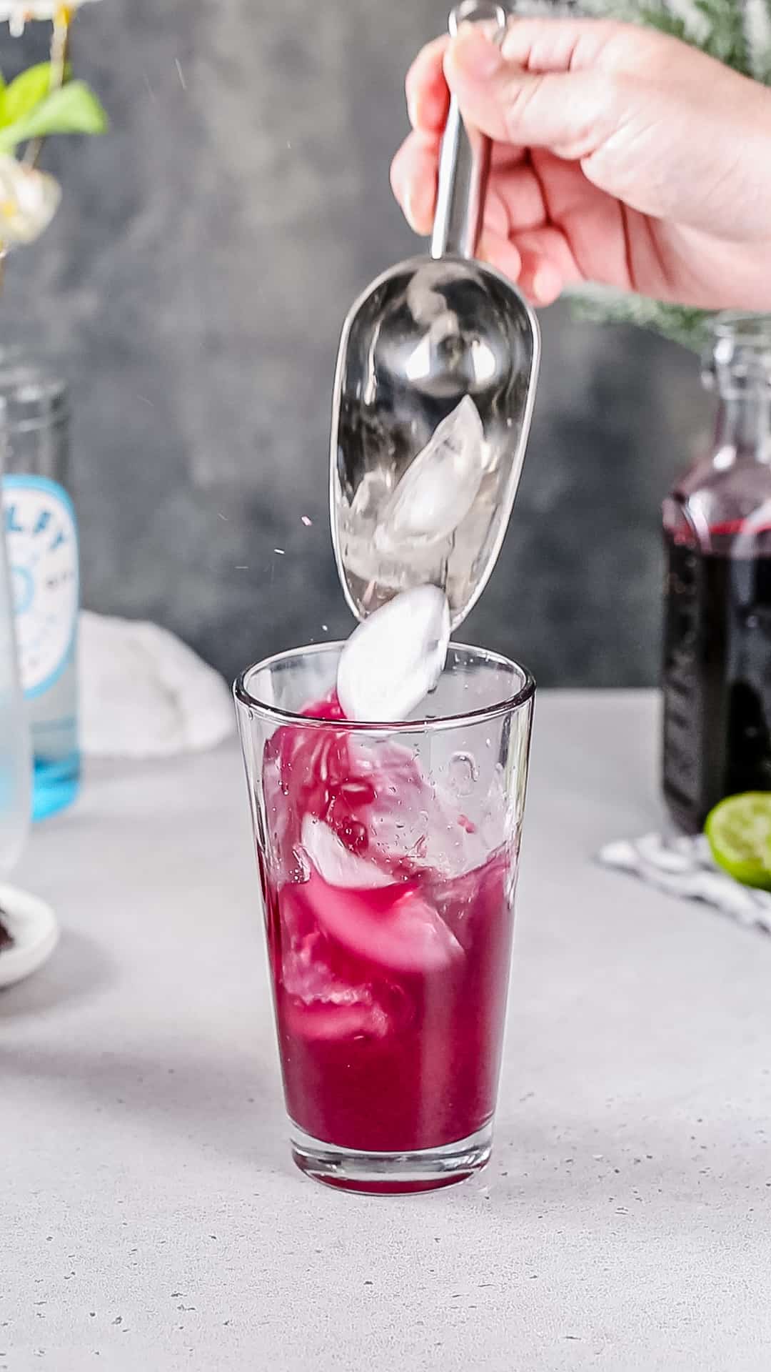 Adding ice to a dark pink cocktail in a glass cocktail shaker.