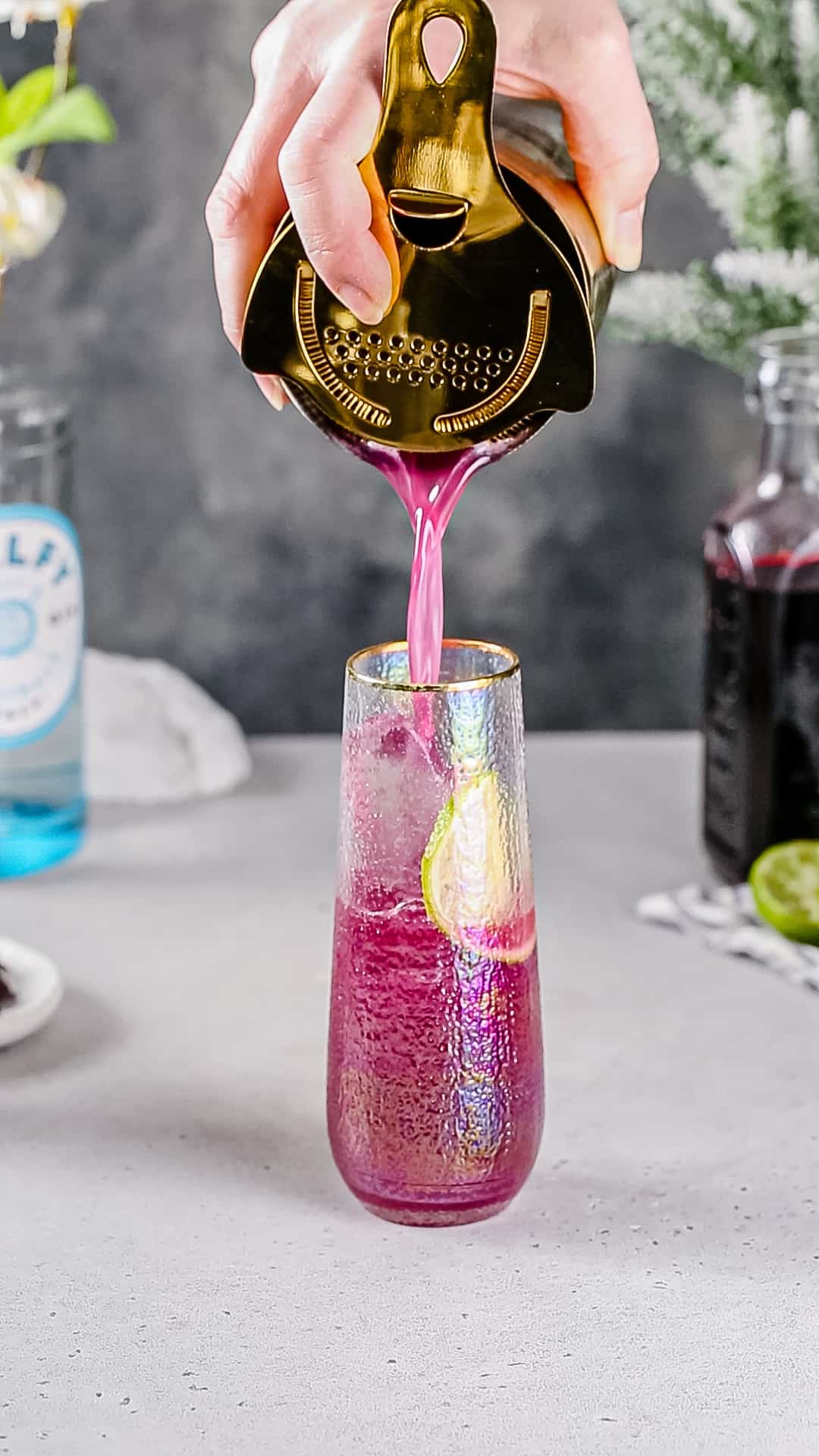 Straining a pink cocktail into a stemless champagne flute filled with ice and a lime wheel.