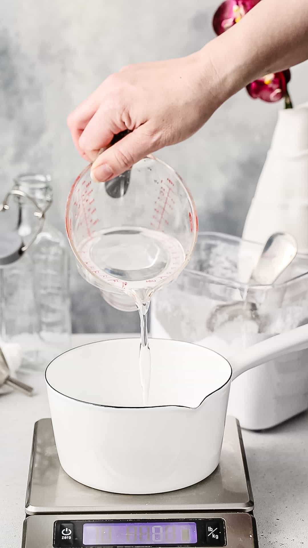 Hand pouring water from a measuring cup into a saucepan.