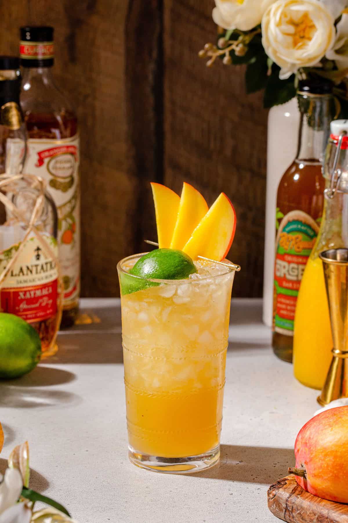 Mango Mai Tai cocktail on a countertop surrounded by bottles and ingredients used to make the drink.