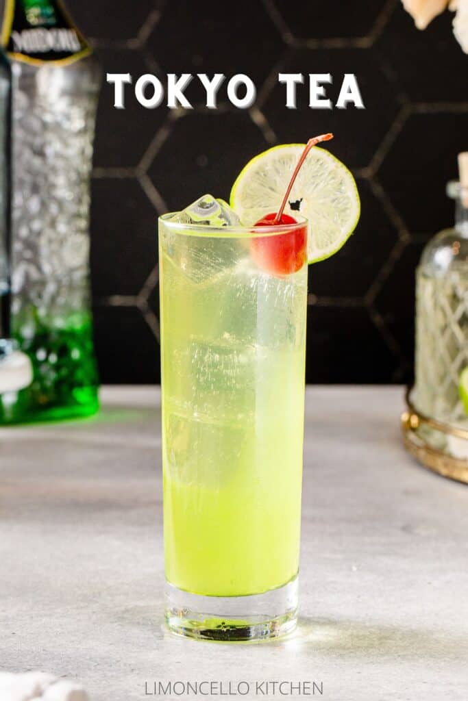 Side view of a Tokyo Tea cocktail, which is chartreuse green in color and has a lime wheel garnish on the rim and a maraschino cherry next to the lime. The cocktail is in a tall glass with straight sides and has ice cubes in it. In the background are a bottle of Midori melon and a bottle of simple syrup. Text saying "Tokyo Tea" is above the drink.
