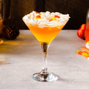 Side view of a Candy Corn Martini with three layers: the top layer is whipped cream, the middle layer is an orange liquid and the bottom layer is a yellow liquid.