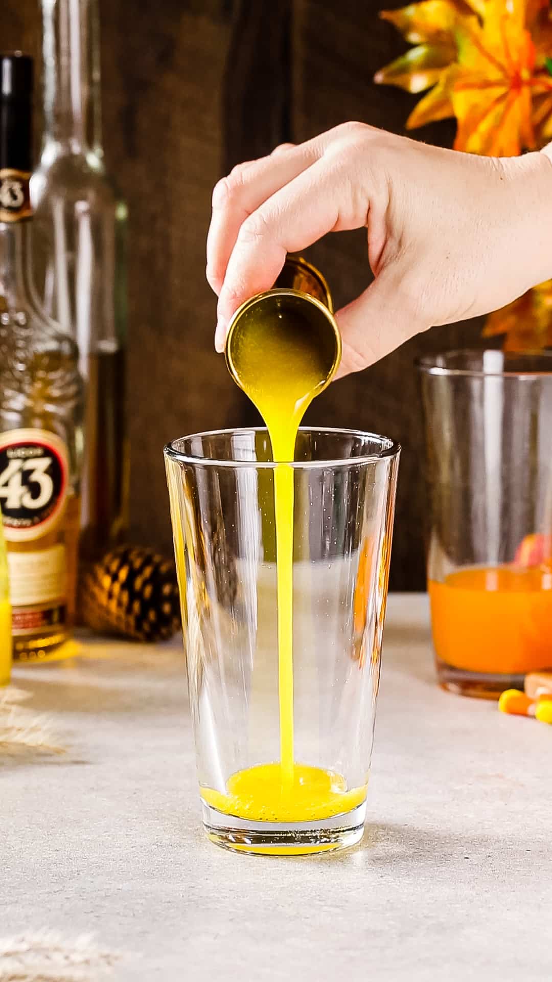 Hand pouring mango nectar into a glass cocktail shaker.