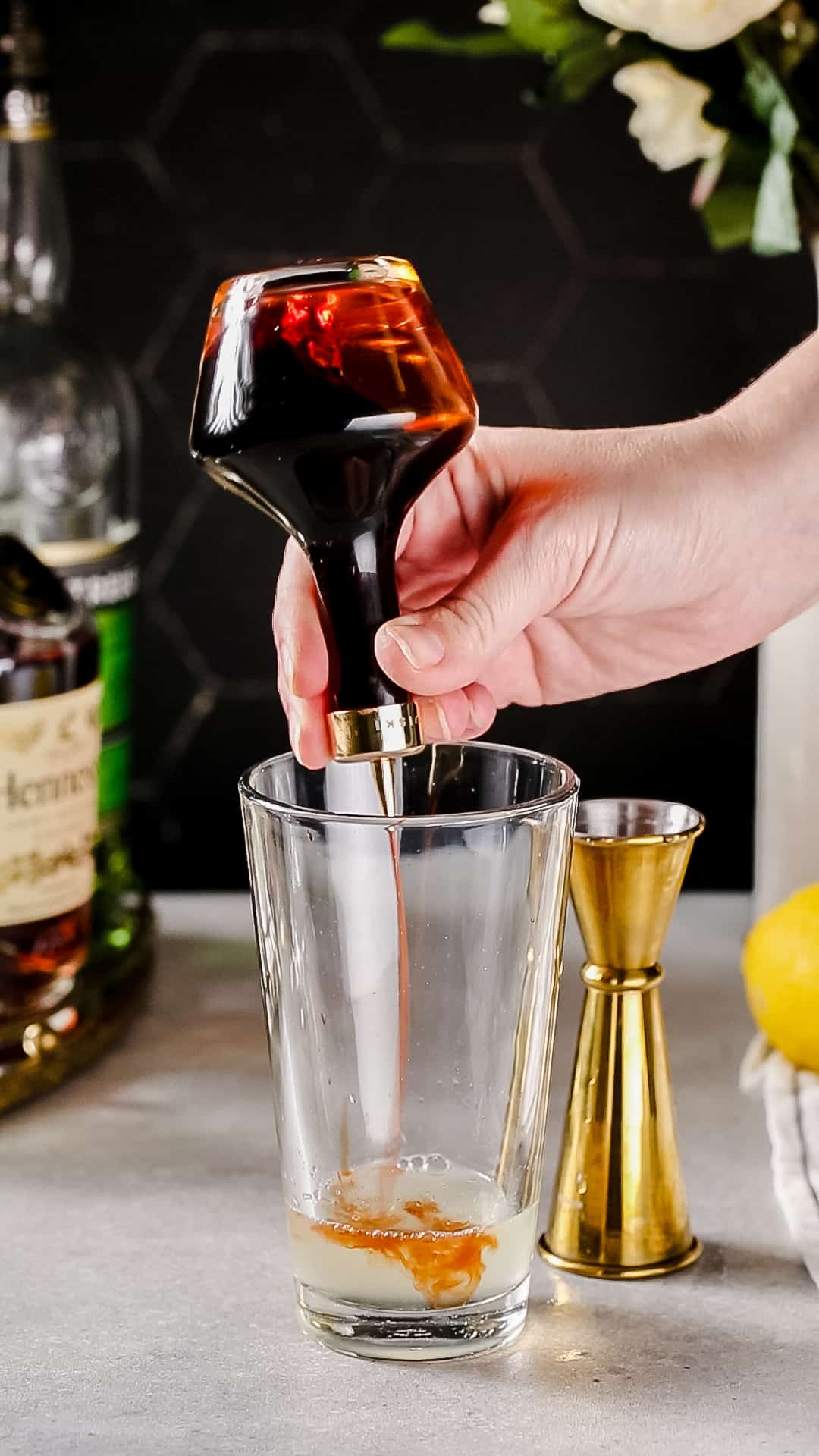 Hand adding Angostura bitters to a cocktail shaker.