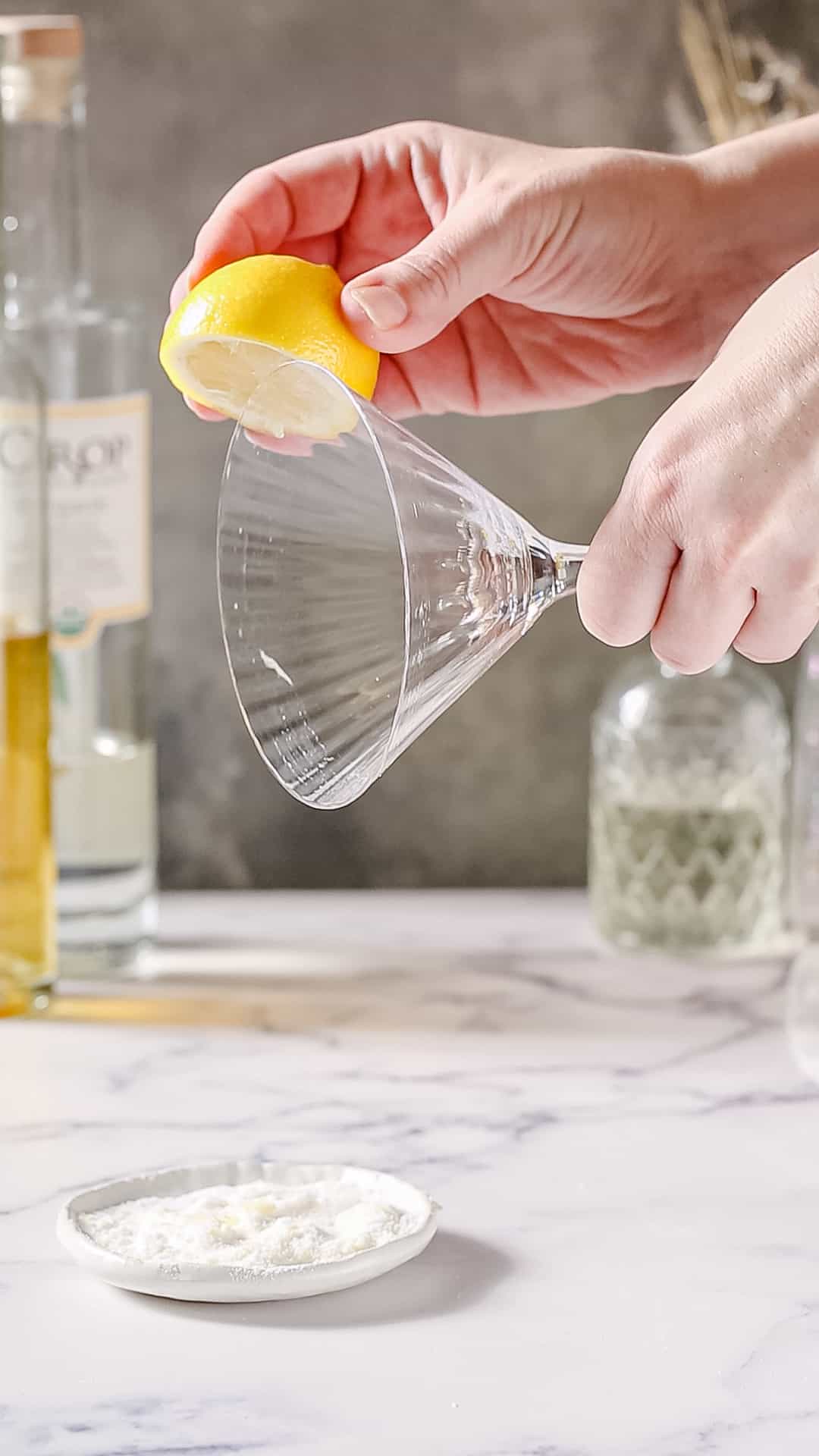 Hand using a cut lemon to wet the rim of a large martini glass.