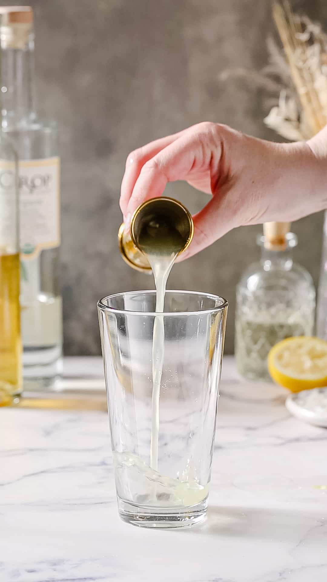 Hand using a jigger to pour lemon juice into a cocktail shaker.