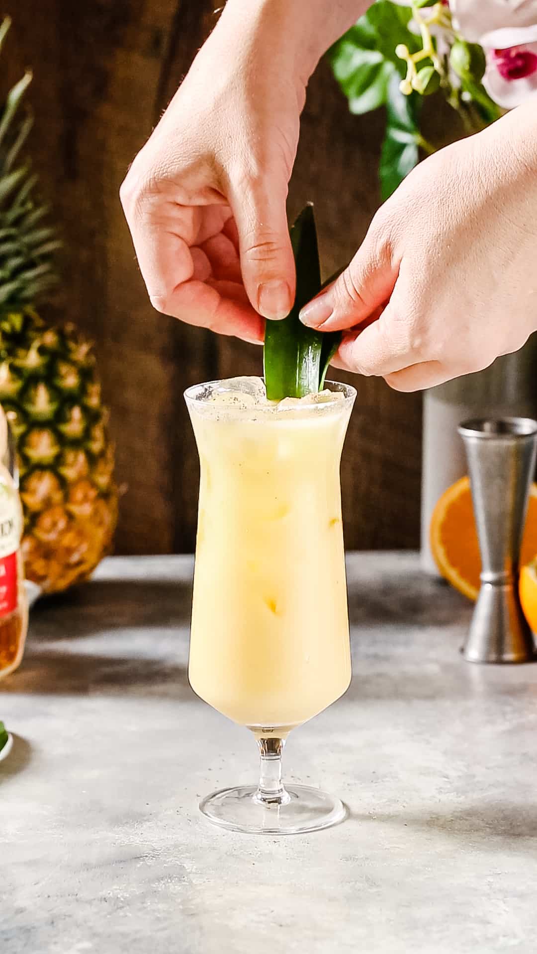 Hands adding pineapple fronds to the cocktail as a garnish.