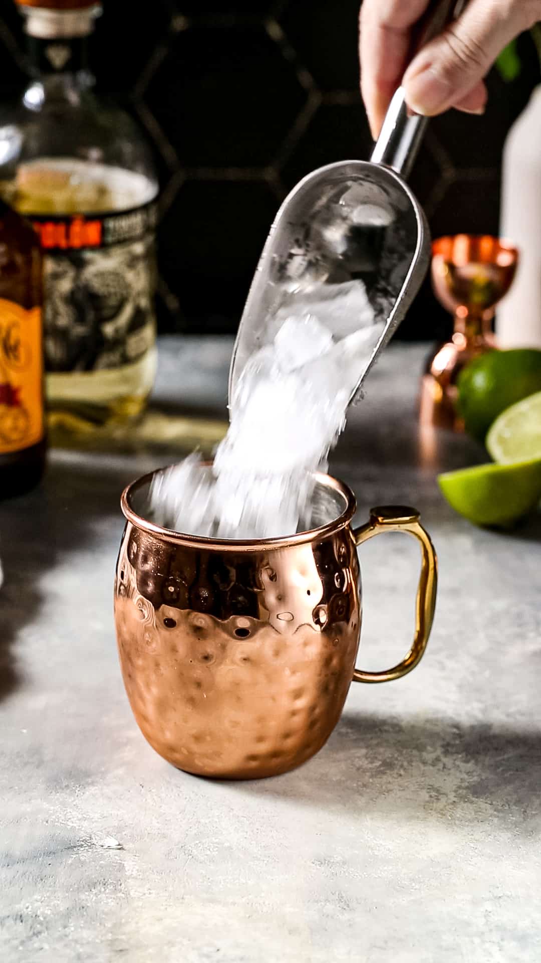 Hand using an ice scoop to add crushed ice to a copper mug.