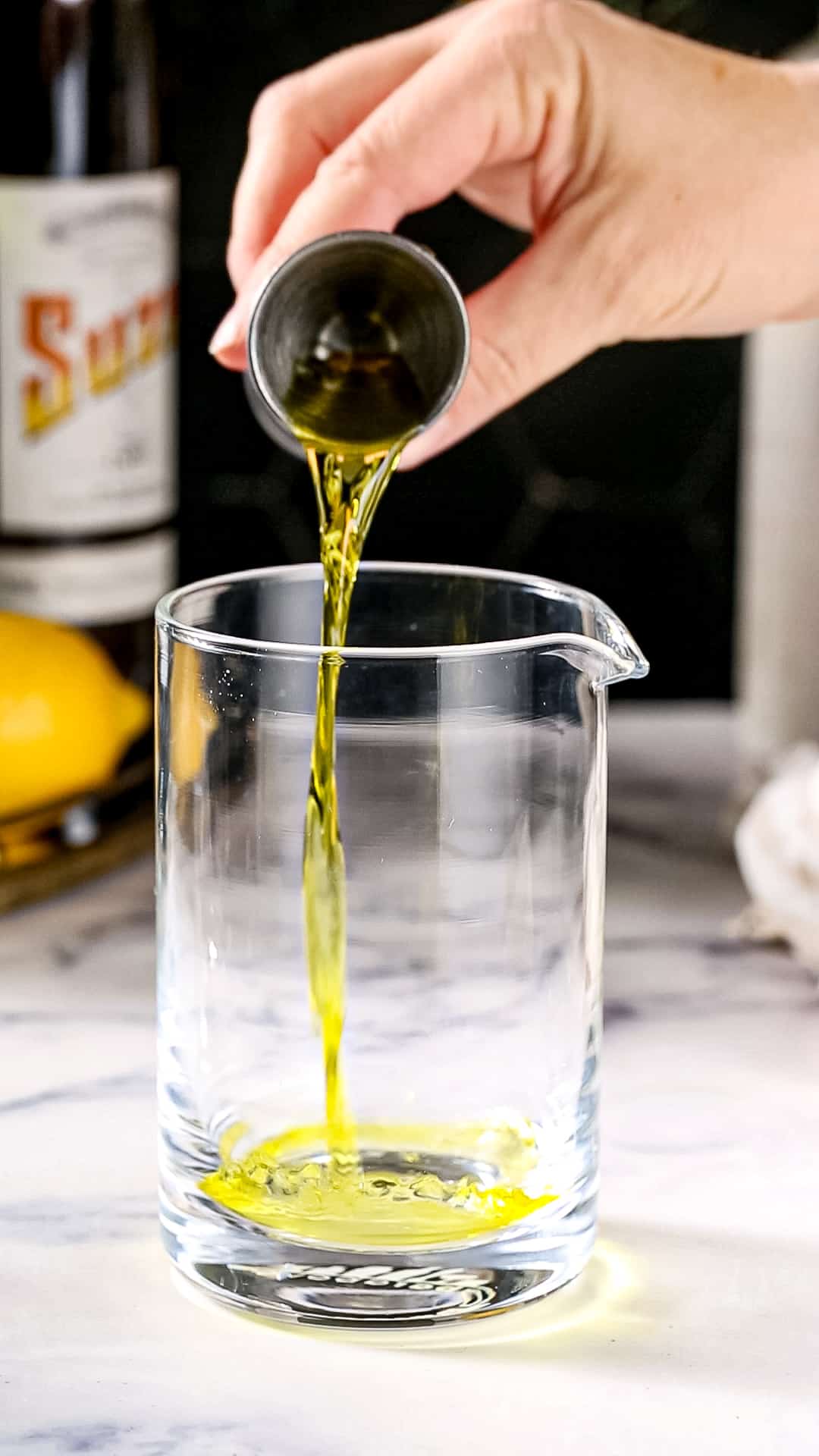 Hand using a jigger to pour Suze liqueur into a mixing glass.