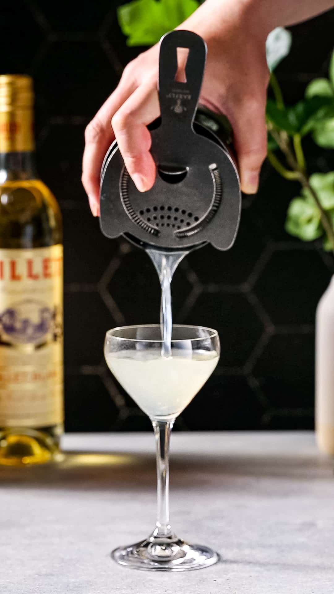 Hand straining a cocktail into a serving glass.