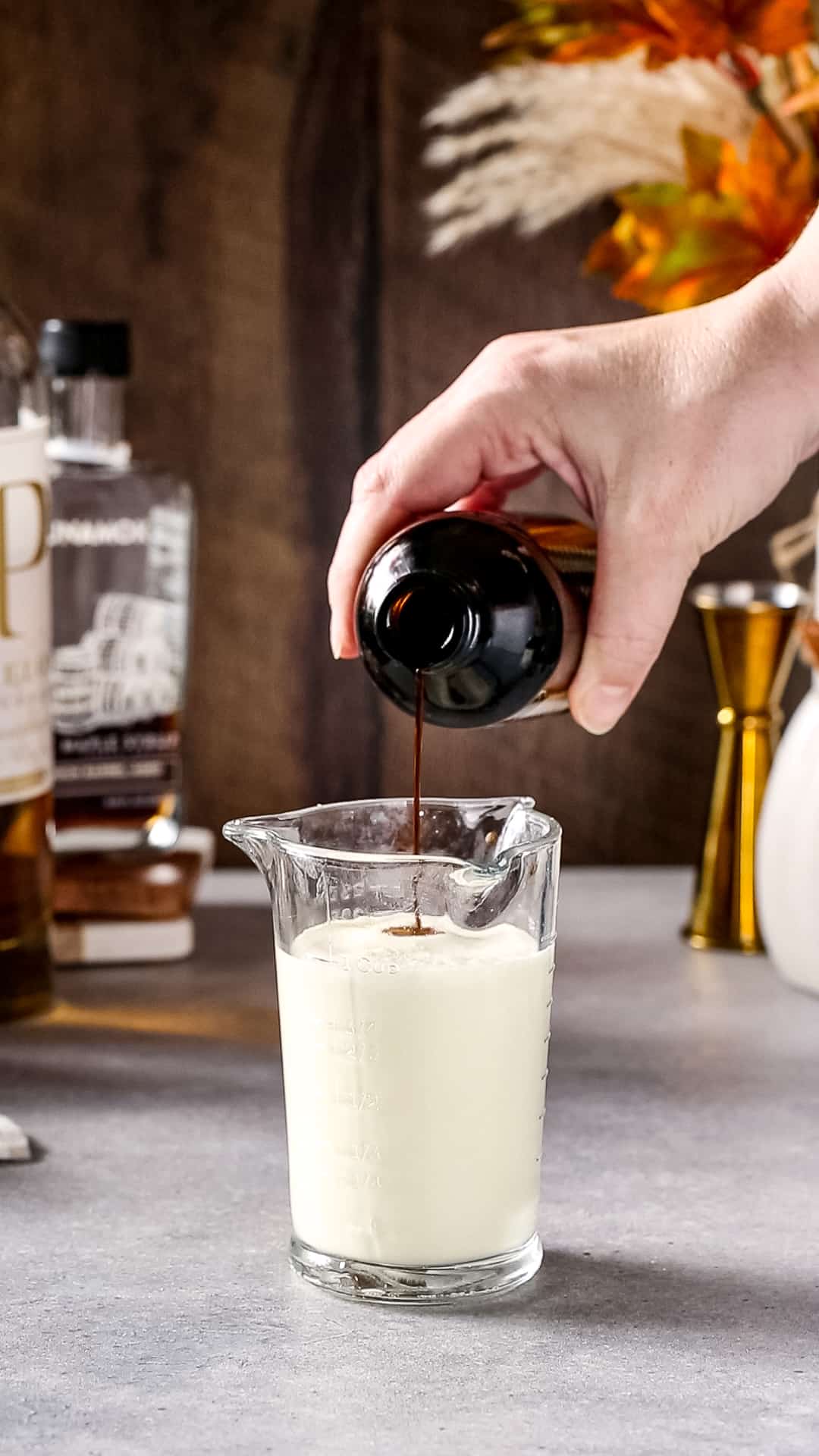 Hand pouring vanilla extract into a measuring cup filled with heavy cream.