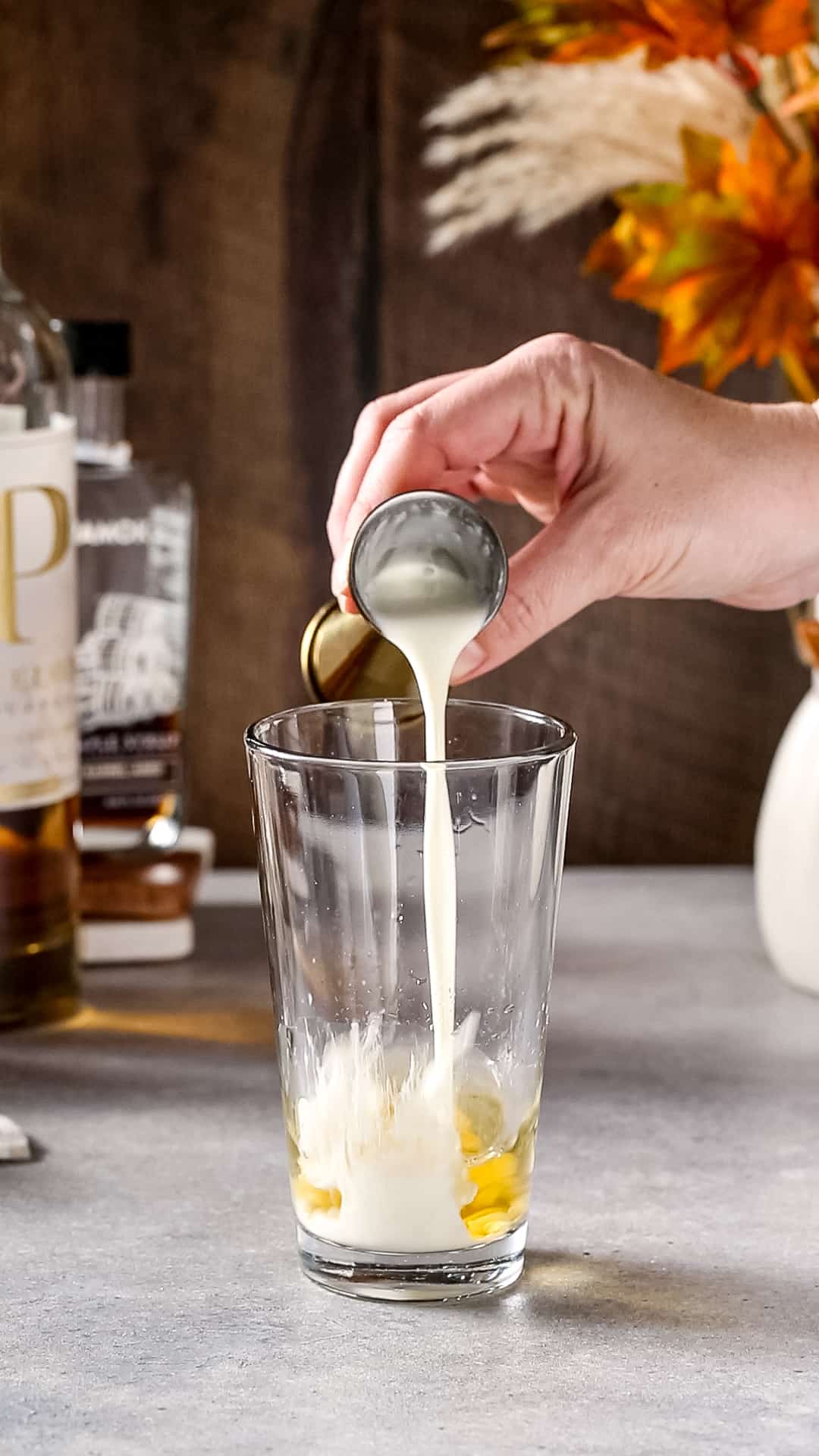 Hand pouring heavy cream into a glass cocktail shaker.