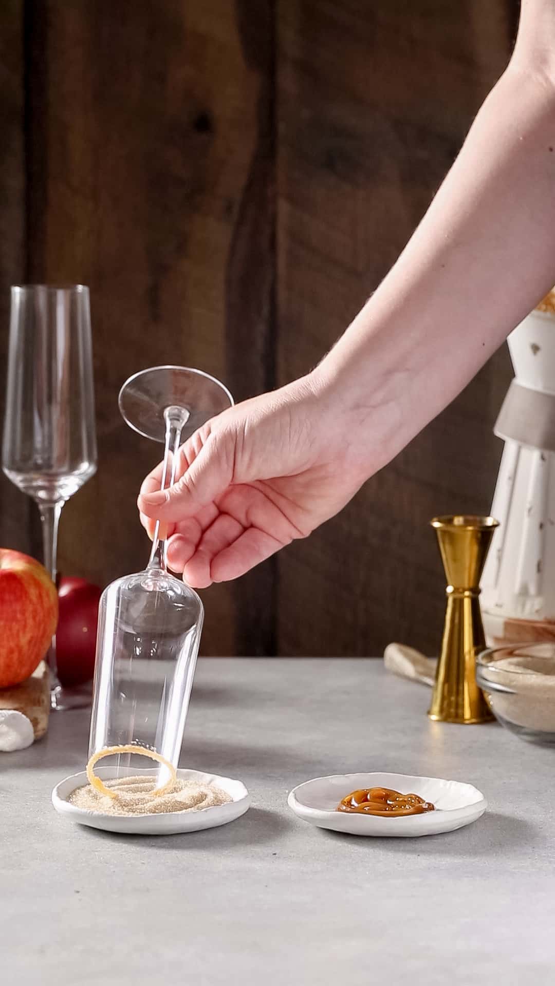 Hand dipping the rim of a champagne flute into a plate of cinnamon sugar.