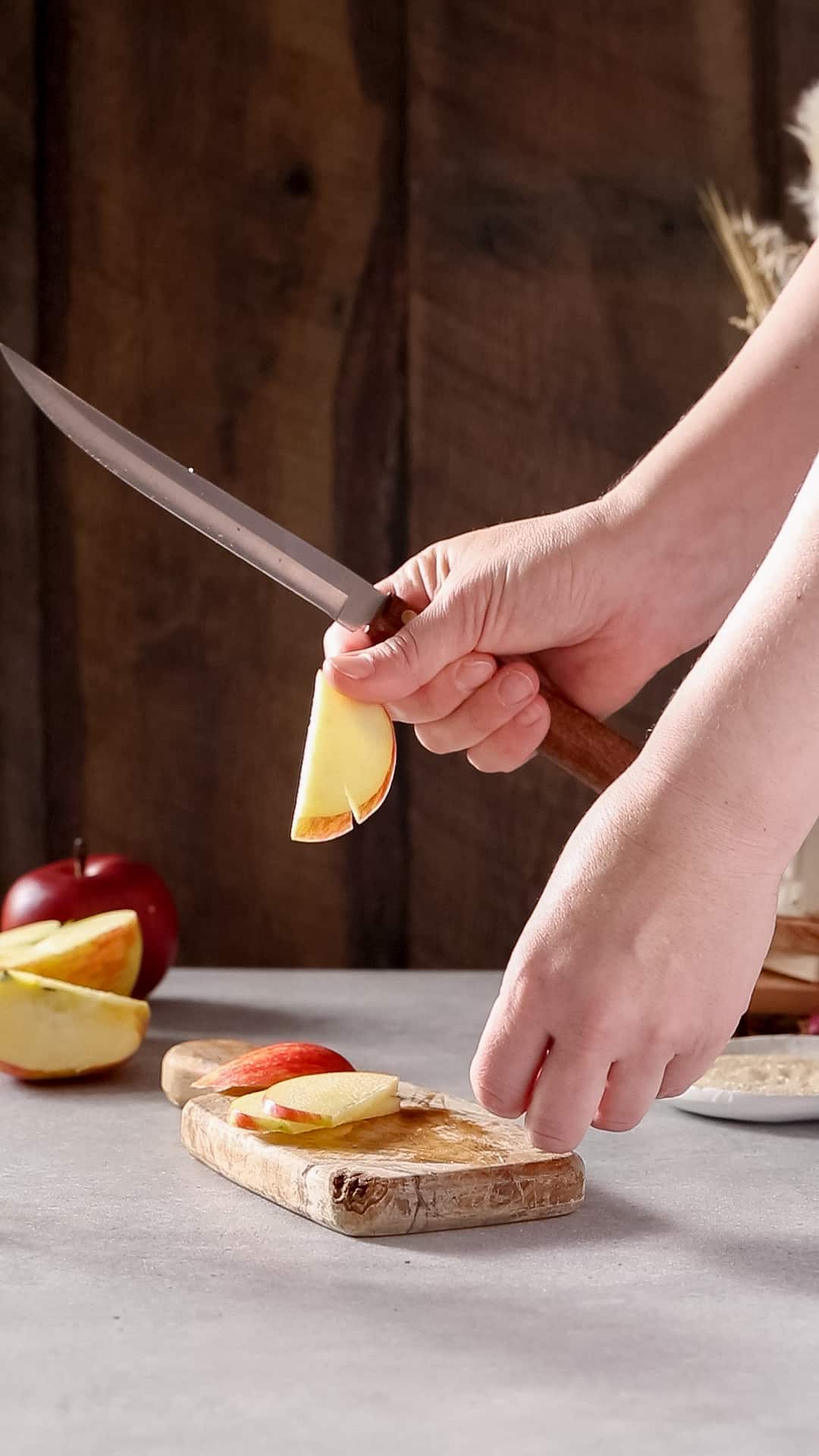 Hand holding up an apple slice that has a notch cut into the side of it. The hand is also holding a wood-handled knife.