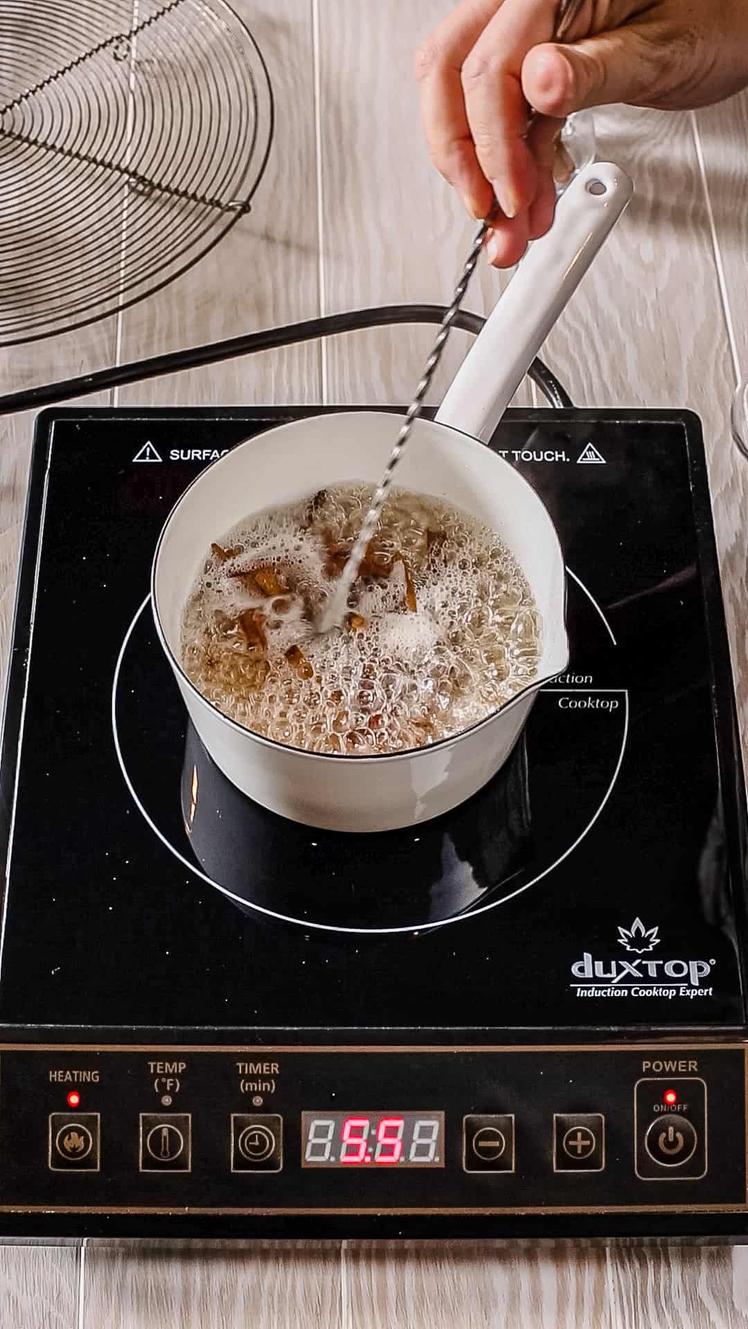 Overhead view of a white saucepan on an induction burner. The liquid is bubbling up.