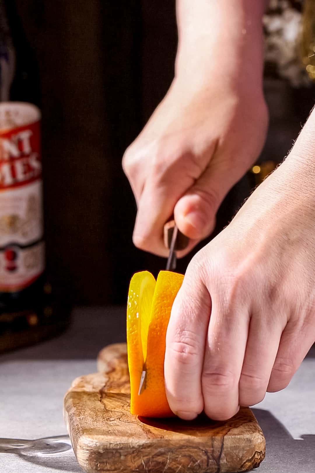 Hands cutting an orange on a cutting board.