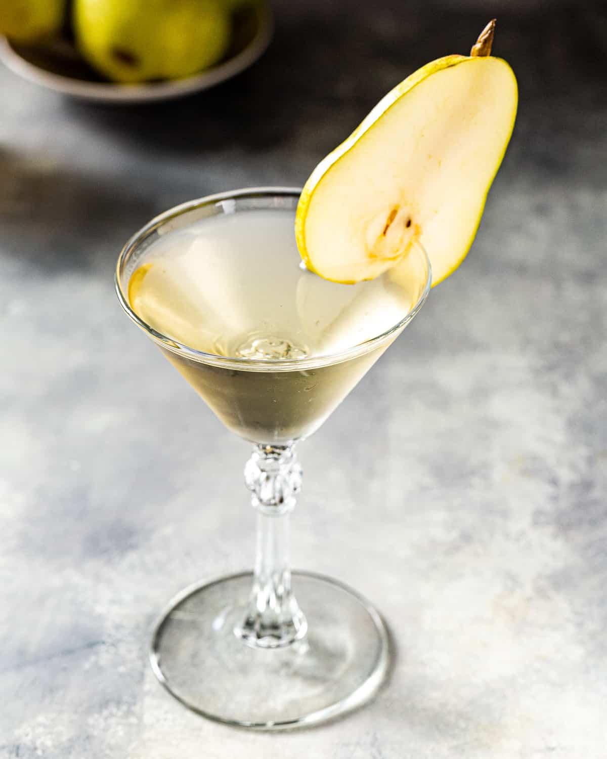 Overhead view of a Pear Martini in a stemmed martini glass with a fresh pear garnish. At the top left of the frame are a couple of fresh pears.