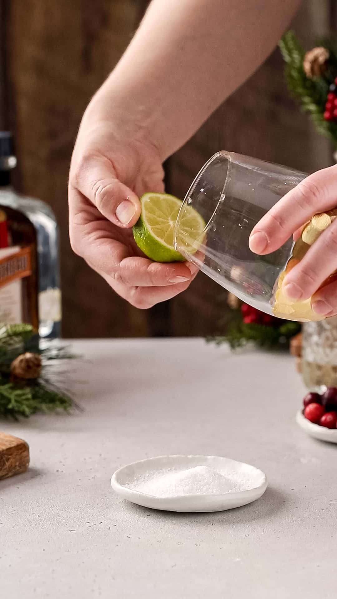 Hands using a cut lime to wet the rim of a gold-bottomed cocktail glass.