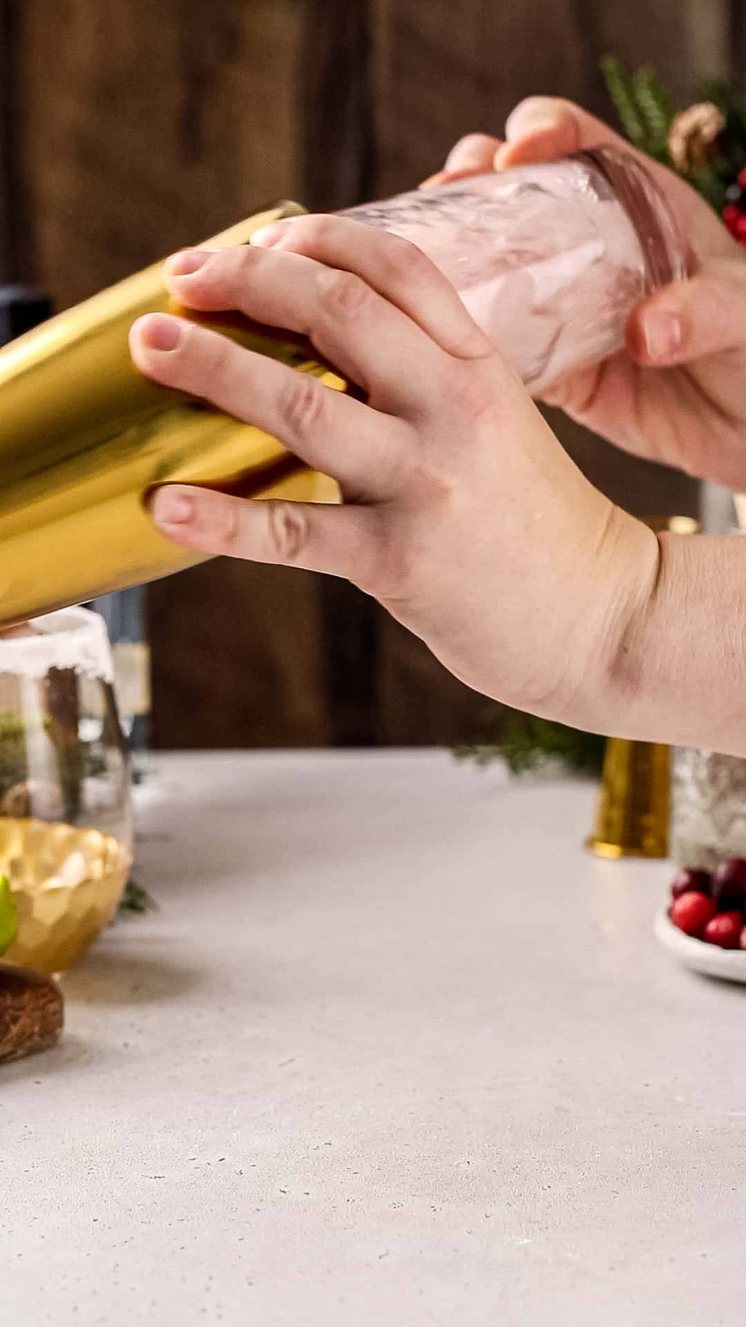 Hands shaking a sealed gold and glass cocktail shaker.