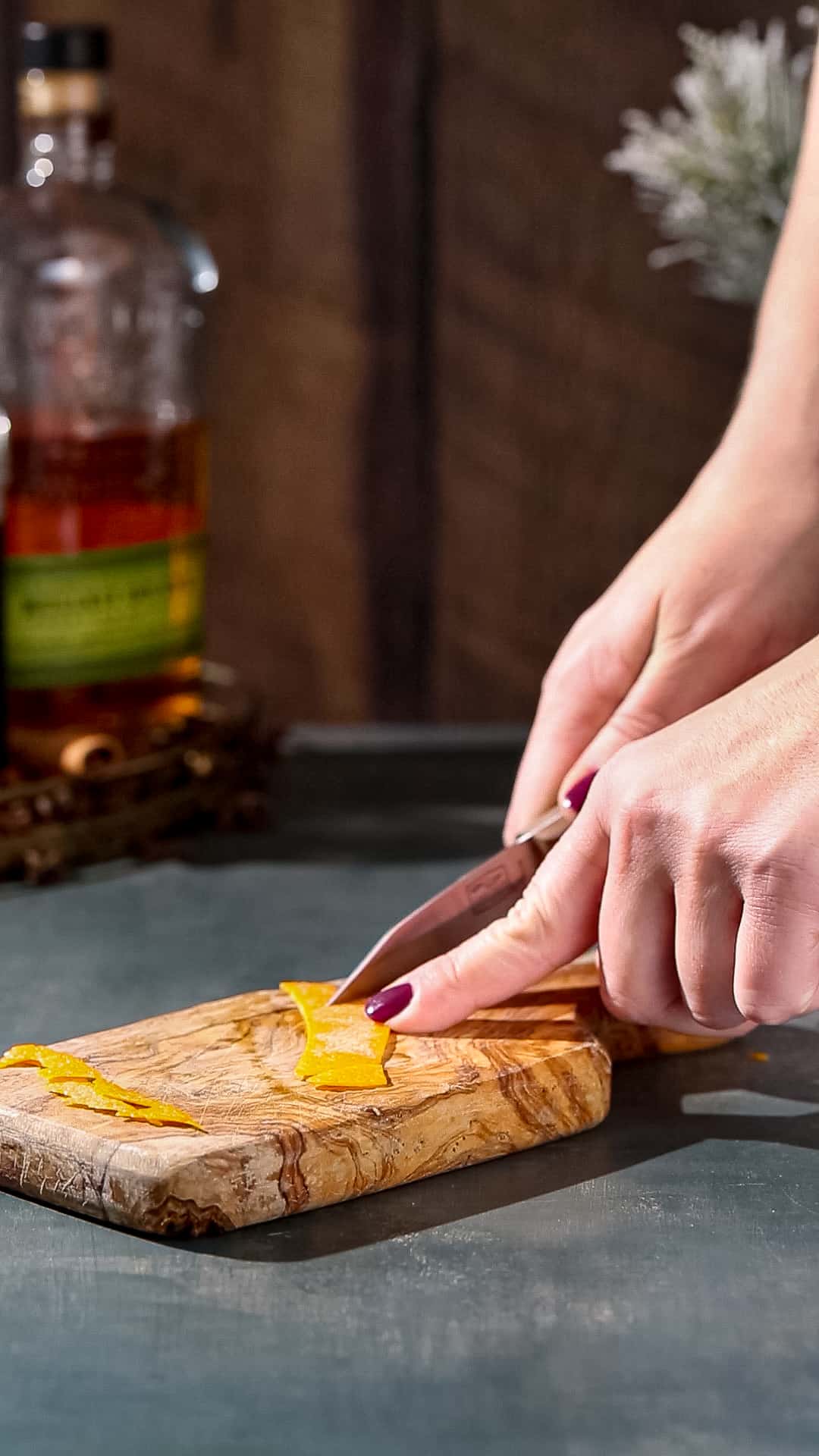 Hands using a paring knife and cutting board to clean up the sides of a piece of orange peel.