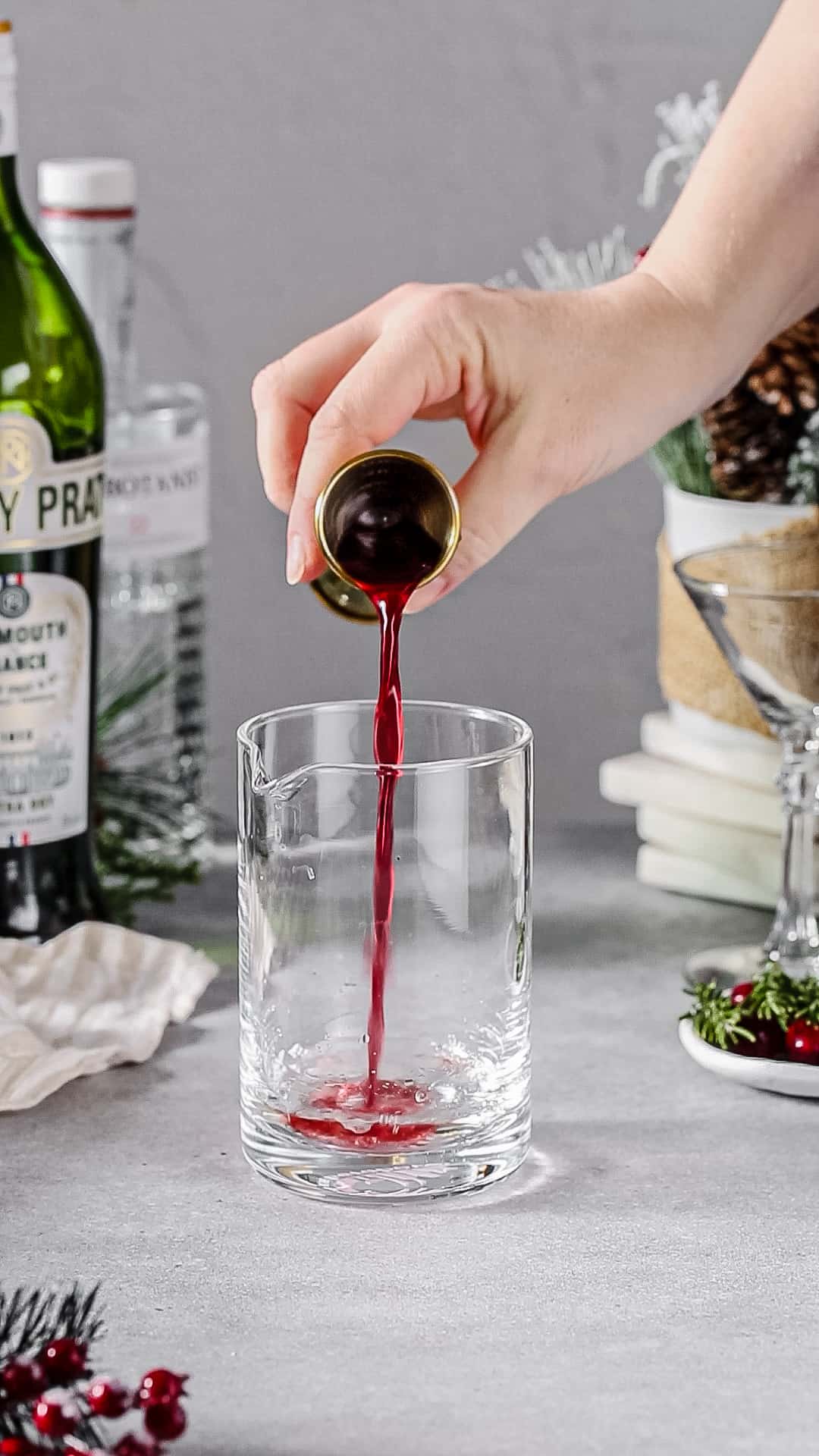 Hand pouring cranberry juice in to a cocktail mixing glass.