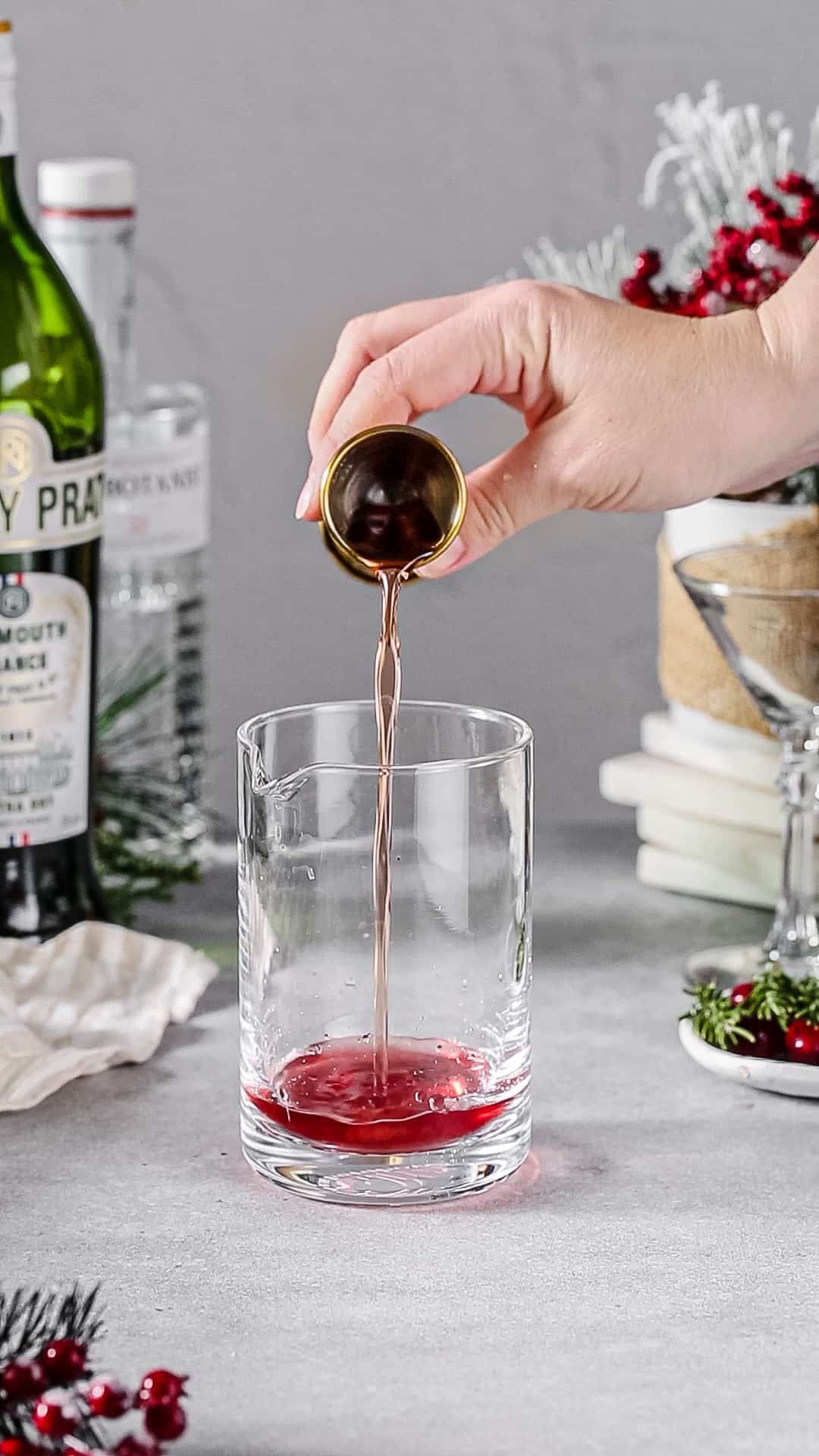 Hand pouring spiced cranberry syrup into a cocktail mixing glass.