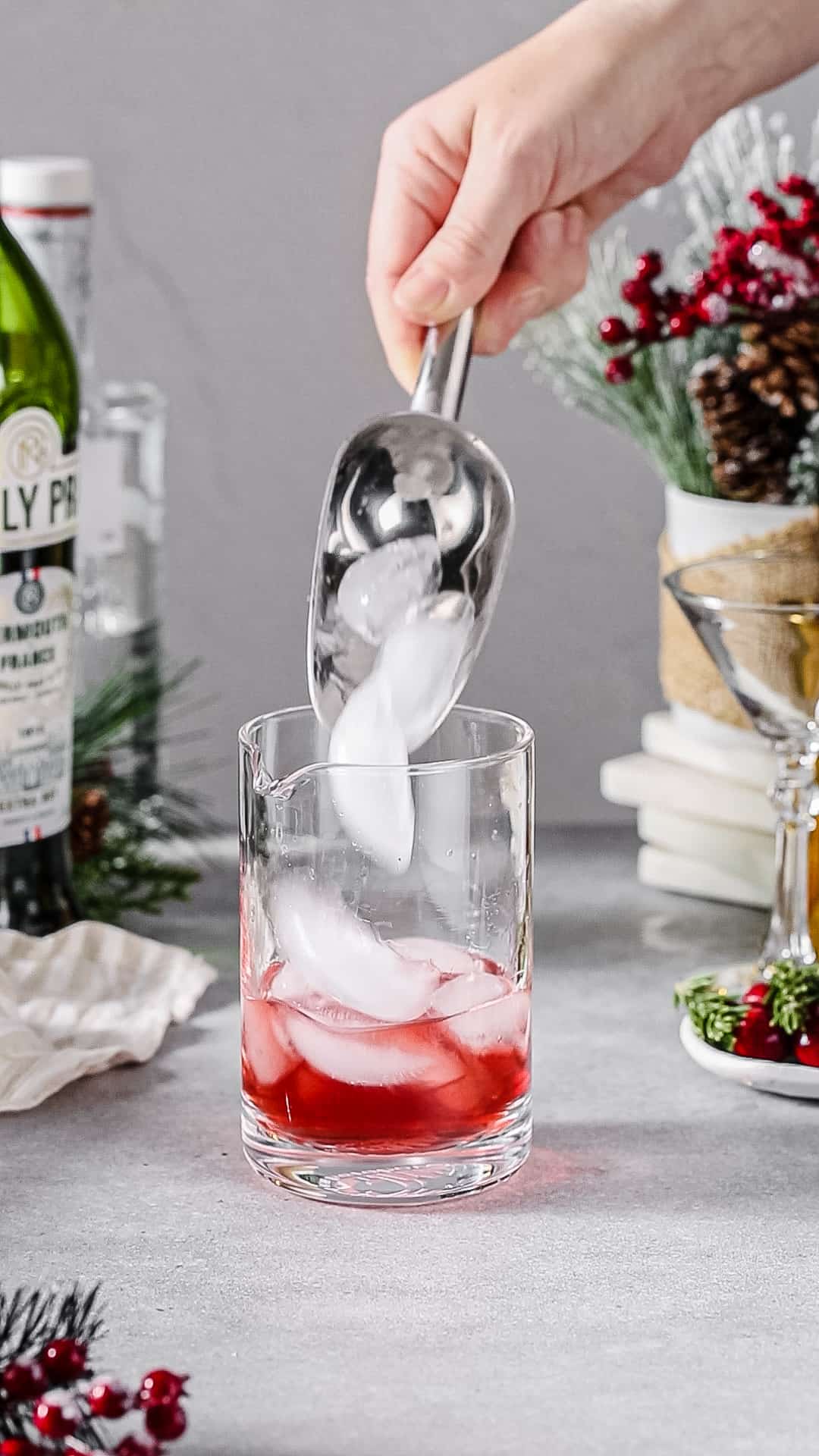 Hand using a silver ice scoop to add ice to a cocktail mixing glass.